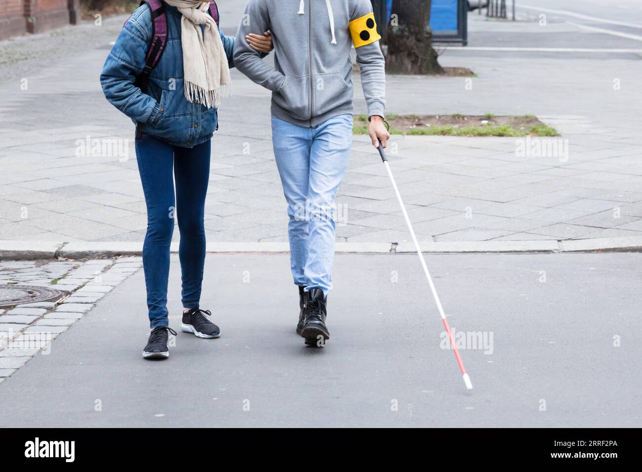 Junge Frau hilft blinden Mann mit weißem Stick beim Überqueren der Straße Stockfoto
