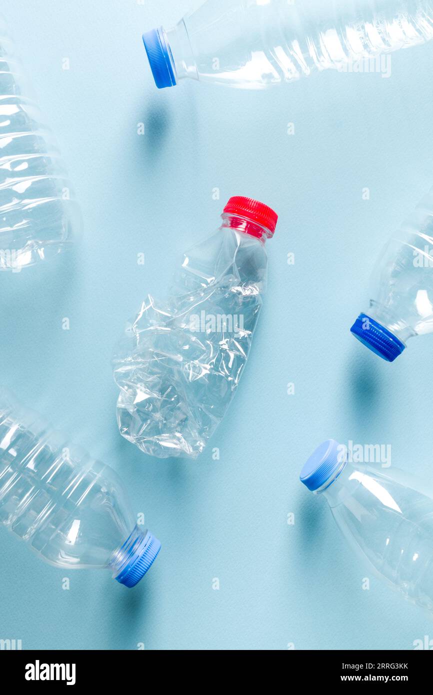 Wasserflaschen aus zerstoßenem Kunststoff mit blauen Kappen, die um die Wasserflasche aus zerstoßenem Kunststoff mit rotem Verschluss auf blauem Hintergrund stehen Stockfoto