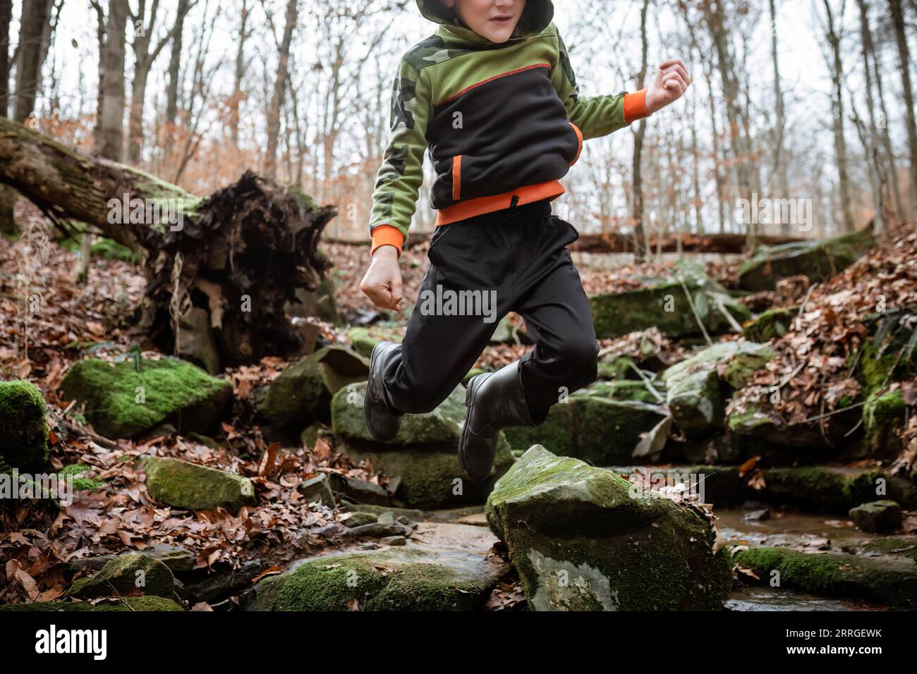 Auf der Herbstwanderung springt das Kind fröhlich über moosbedeckte Felsbrocken Stockfoto