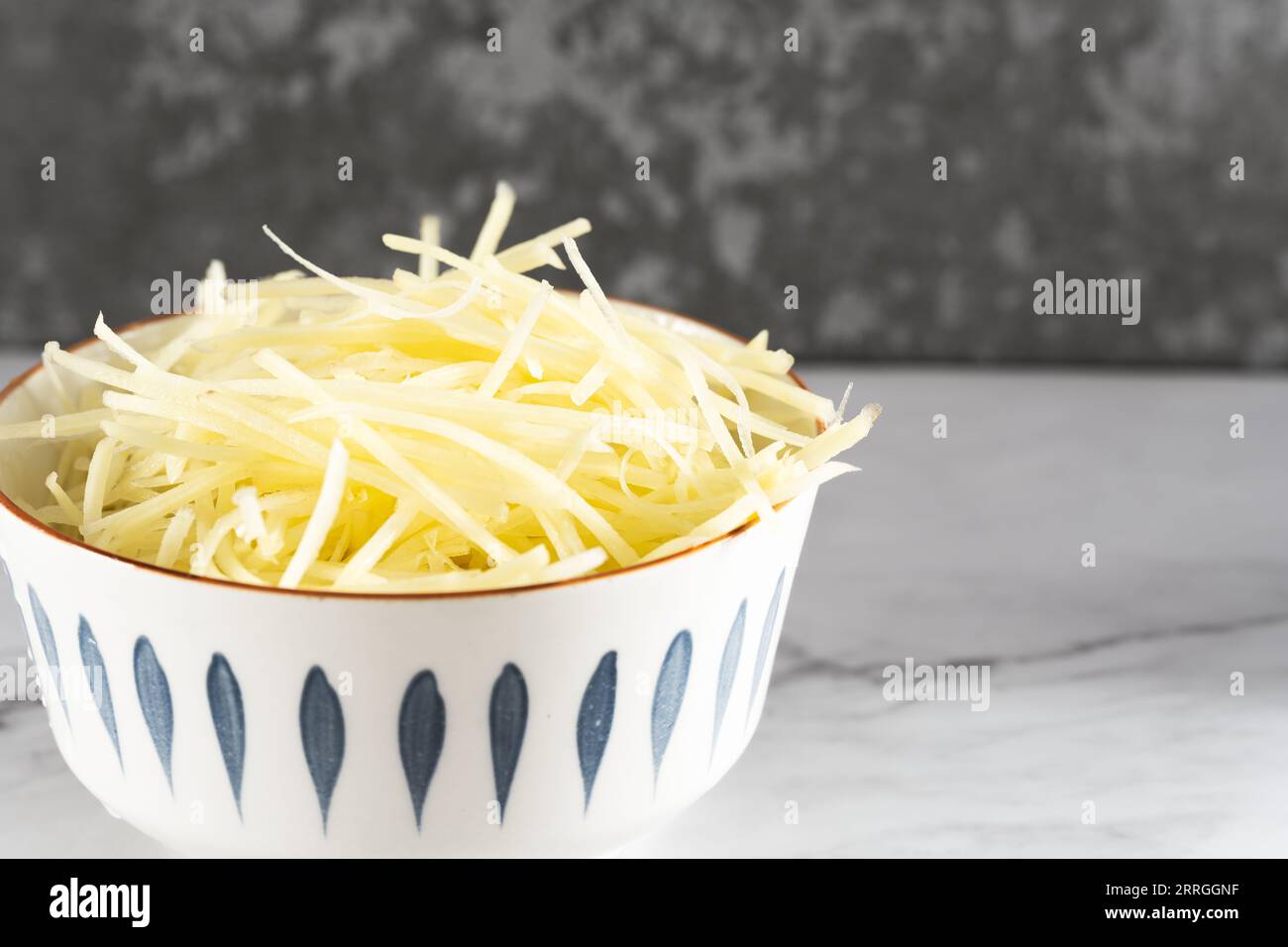 Das Sonnenlicht beleuchtet die Schüssel mit geschnittenen Kartoffelfetzen auf einer geschnittenen Marmorplatte. Stockfoto