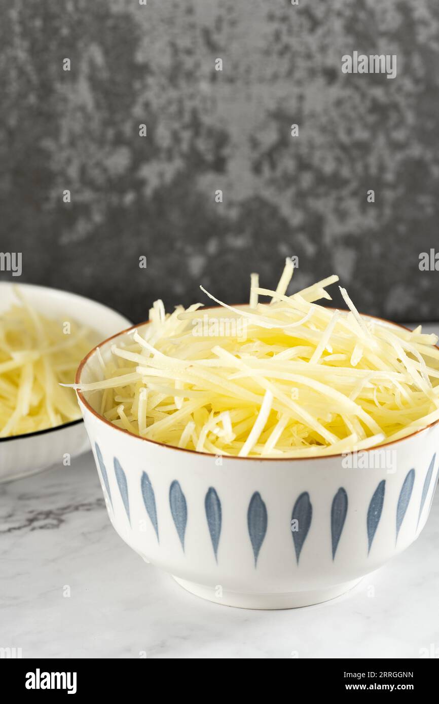 Das Sonnenlicht beleuchtet die Schüssel mit geschnittenen Kartoffelfetzen auf einer geschnittenen Marmorplatte. Stockfoto
