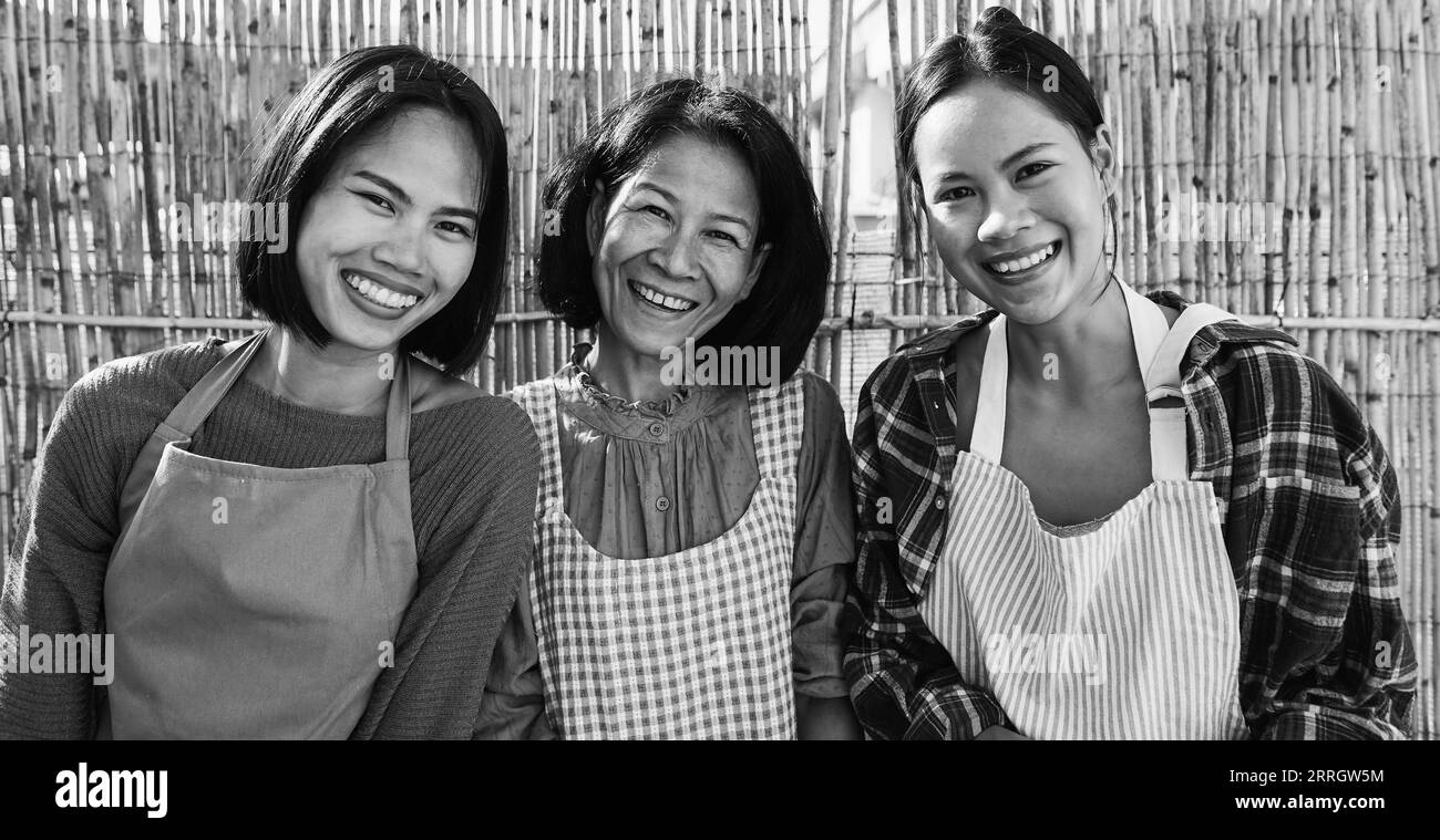Asiatische Mutter mit Töchtern, die vor der Kamera lächeln auf der Terrasse zu Hause - fröhliche Familienkost im Freien am Sommertag - Schwarzweiß-Bearbeitung Stockfoto