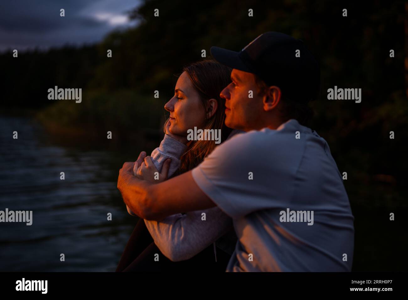 Ein junges kaukasisches Paar, das einen wunderschönen Sonnenuntergang über einem ruhigen See genießt. Stockfoto