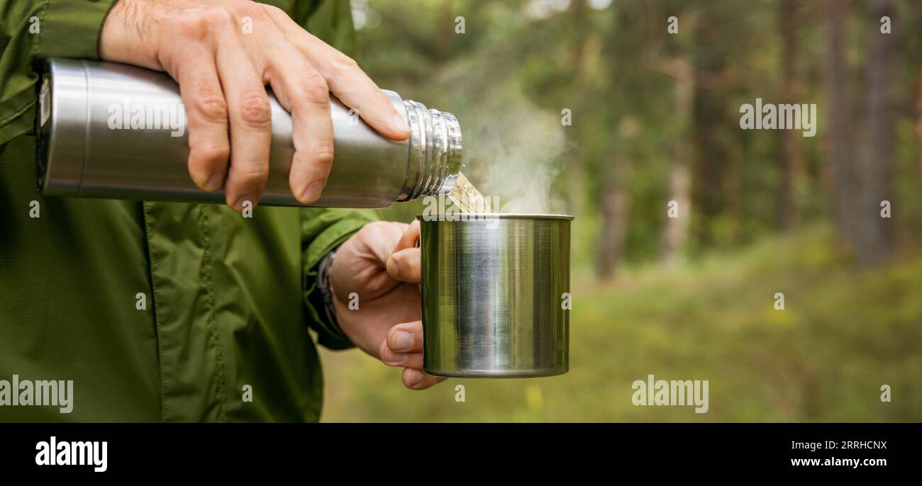 Der Mensch gießt heißen Tee aus Thermoskanne in einen Becher im Wald. Naturtourismus und Camping-Konzept. Banner mit Kopierraum Stockfoto