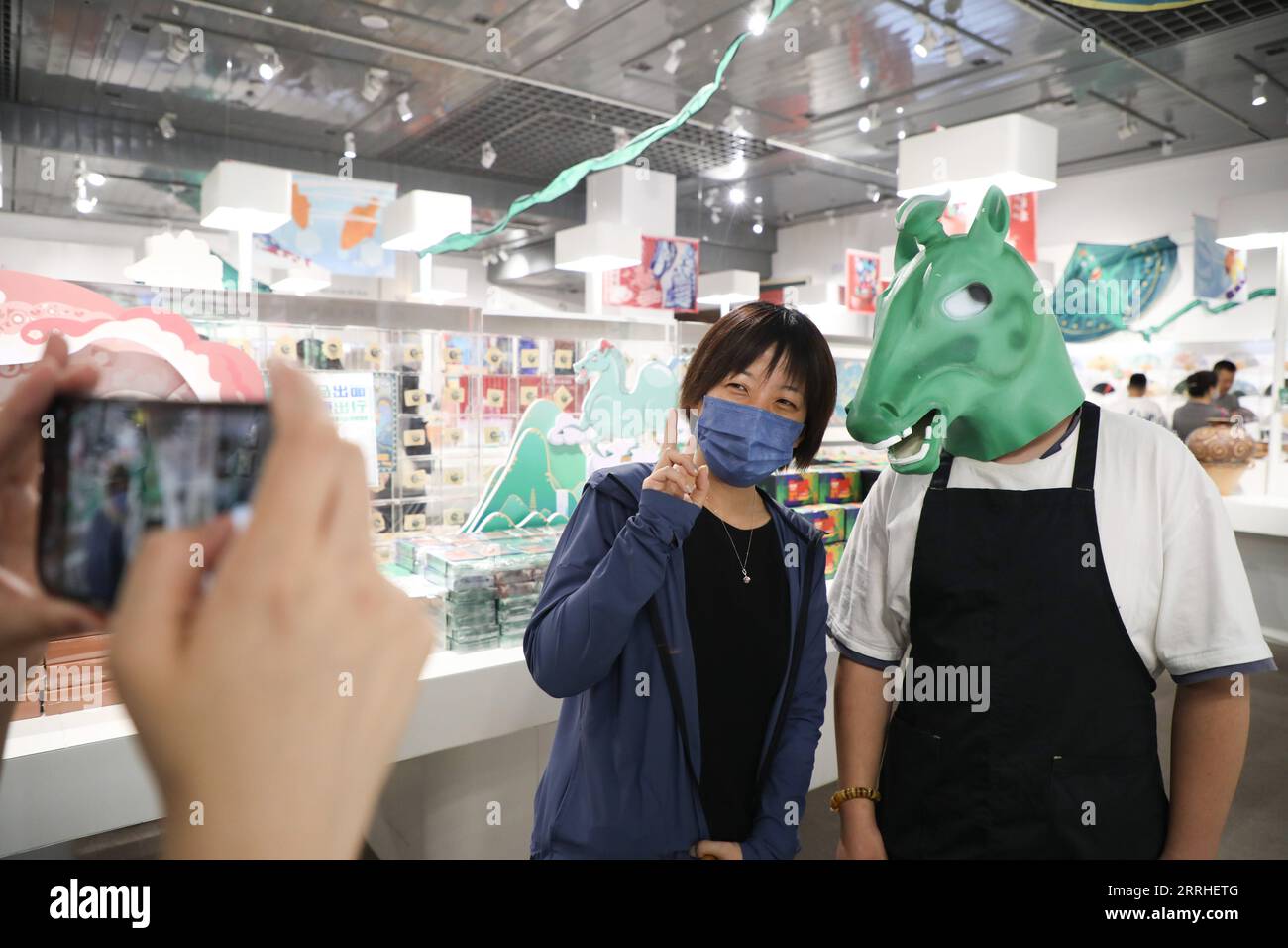 220628 -- LANZHOU, 28. Juni 2022 -- Ein Tourist L posiert für Fotos mit einem Mitarbeiter, der Kopfbedeckung trägt und eine alte Bronzestatue zeigt, in einem Geschäft im Gansu Provincial Museum in Lanzhou, der Hauptstadt der nordwestchinesischen Provinz Gansu, am 28. Juni 2022. Die bronzene Pferdestatue, bekannt als Bronze Galloping Horse tretend auf einer fliegenden Schwalbe, wurde in den 1960er Jahren aus dem Leitai-Grab der östlichen Han-Dynastie 25-220 n. Chr. in Wuwei entdeckt und ist heute im Provinzmuseum Gansu erhalten. CHINA-GANSU-MUSEUM-KULTUR- UND KREATIVPRODUKT CN MAXXIPING PUBLICATIONXNOTXINXCHN Stockfoto