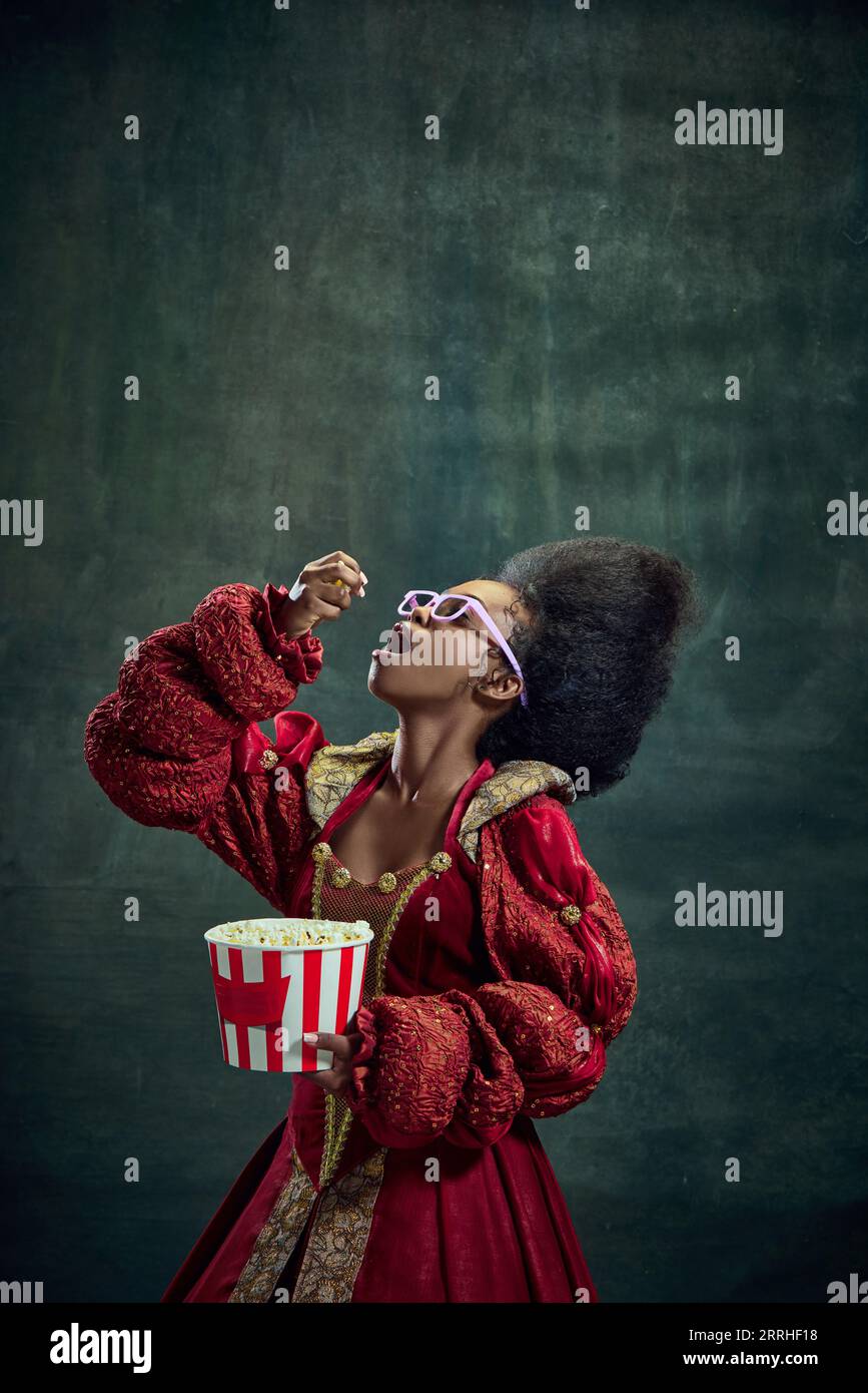 Filmabend. Afrikanisches junges Mädchen, mittelalterliche Prinzessin, die Popcorn vor altem grünem Hintergrund isst. Historische Darstellung Stockfoto