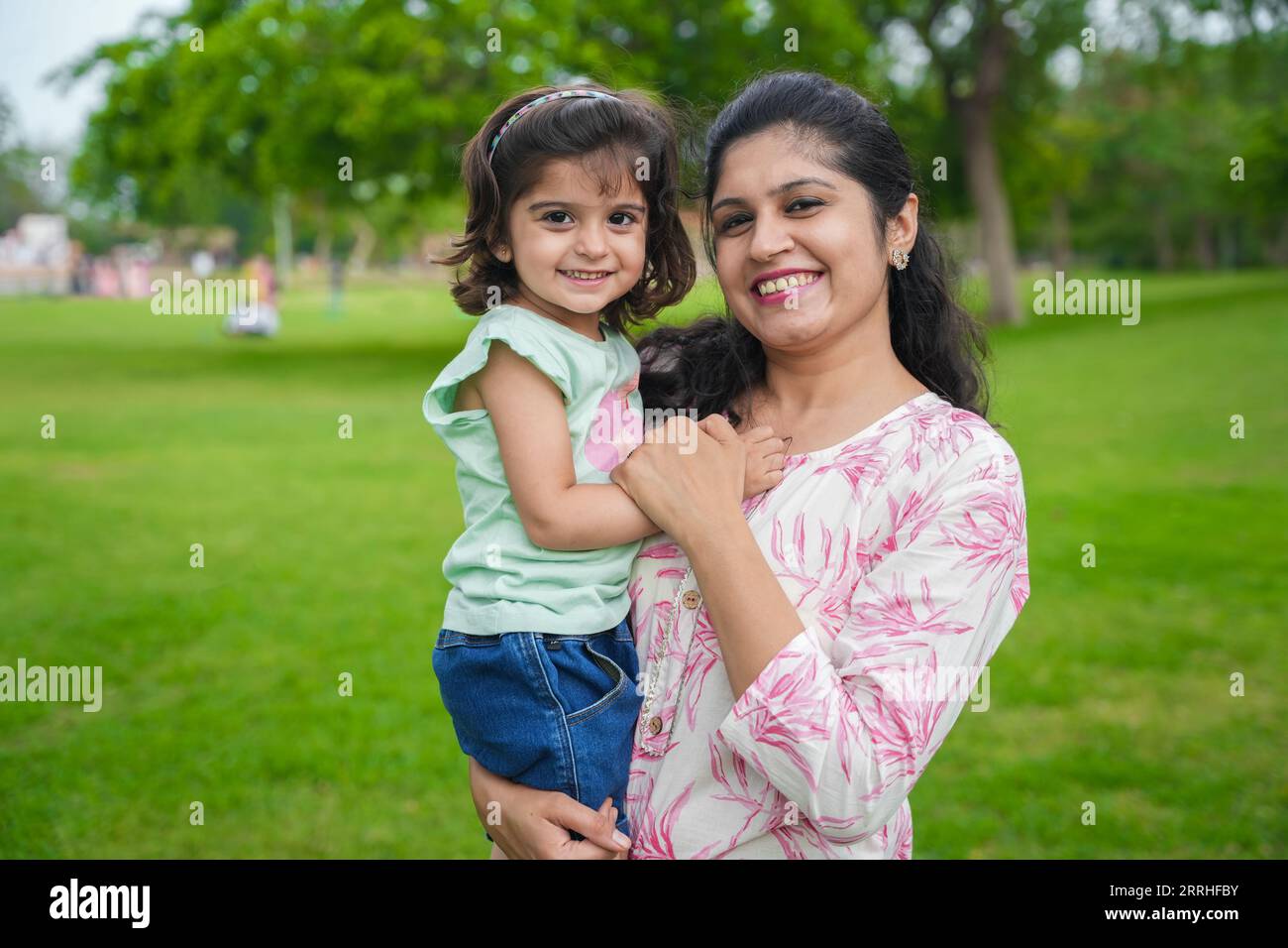 Porträt der glücklichen jungen indischen Mutter und der süßen kleinen Mädchentochter im Sommerpark oder Garten. Stockfoto