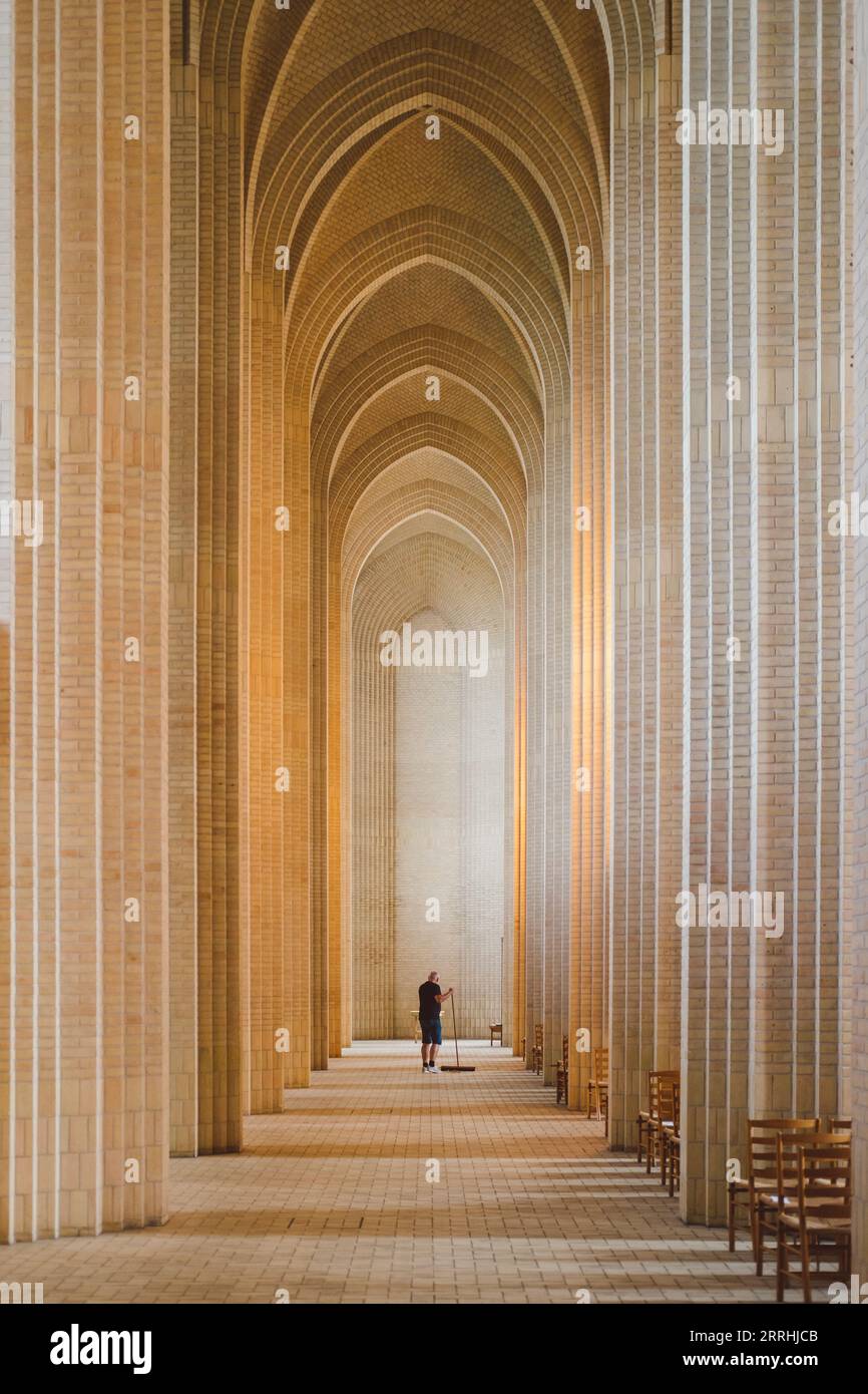 Eine einzige kleine Figur eines Mannes in der Mitte des Grundtviger Kirchenkorridors, der den Boden reinigt Stockfoto