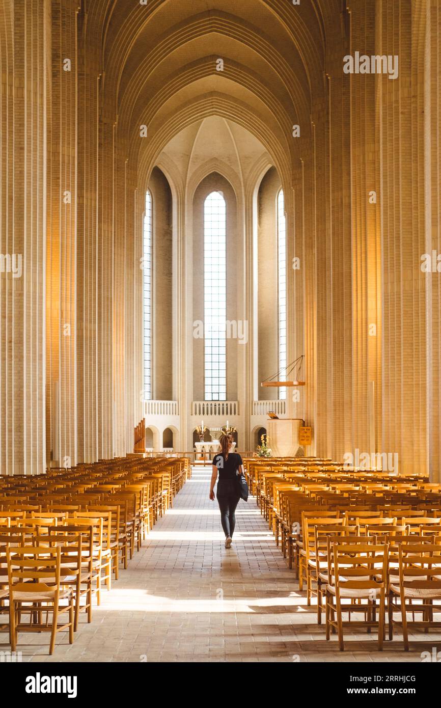 Eine Frau geht in der Mitte des senkrechten Mittelteils der Grundtviger Kirche in Richtung des Heiligtums mit extrem hohen Fenstern und Säulen Stockfoto