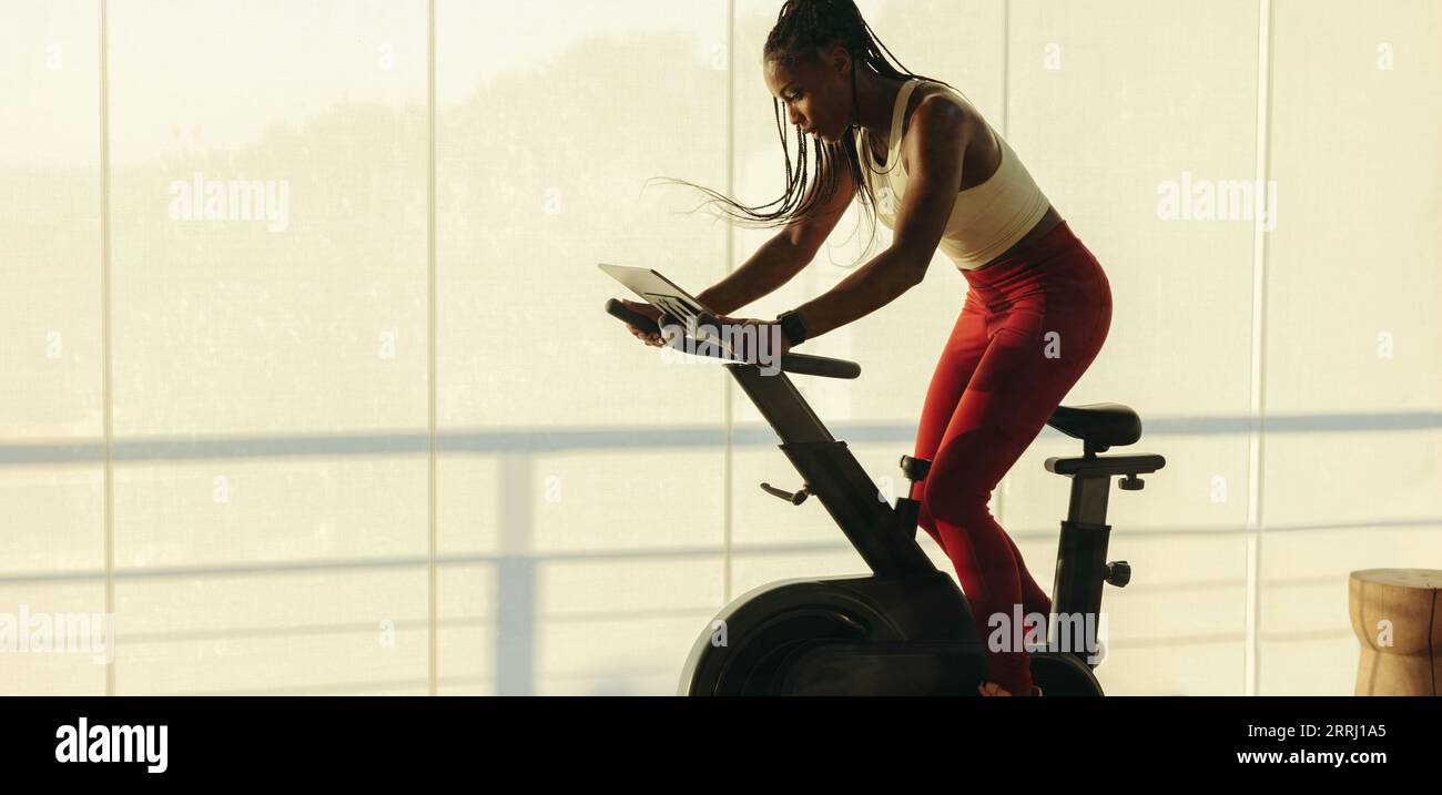 Junge Frau, die sich mit einem smarten Heimtrainer und einer Fitness-App für das Indoor-Radfahren in ihr Heimtraining einmischt. Schwarze Buchse mit High-Tech-Fitn Stockfoto