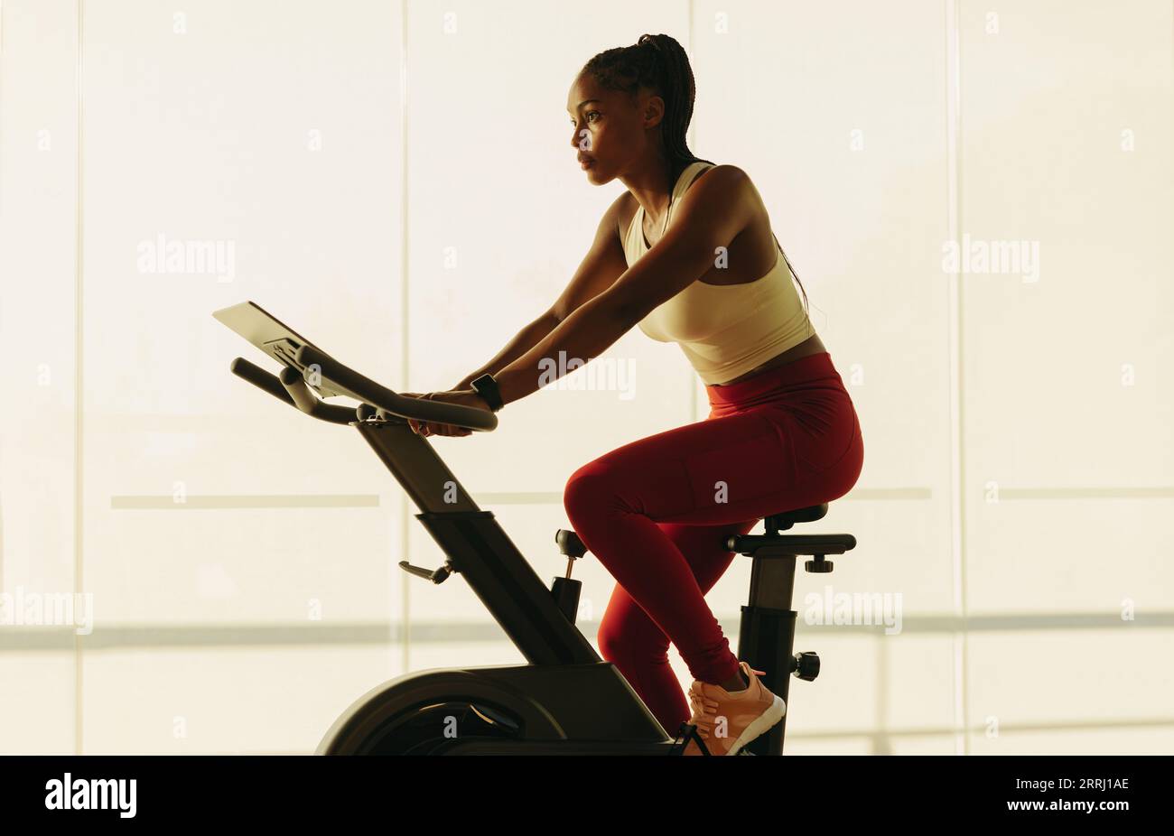 Sportliche schwarze Frau, die sich in ein gesundes Home-Workout-Routine, mit einem Heimtrainer als Teil ihres Fitness-Regimes. Junge Frau, die mit einem trainiert Stockfoto