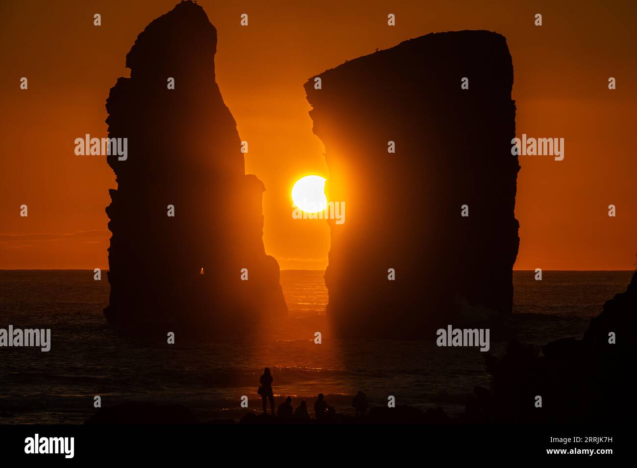 Junge Leute treffen sich, um die riesigen Meeresstapel zu beobachten, die vom Sonnenuntergang auf Ponta dos Mosteiros in Sao Miguel, Azoren, Portugal, umrahmt werden. Stockfoto