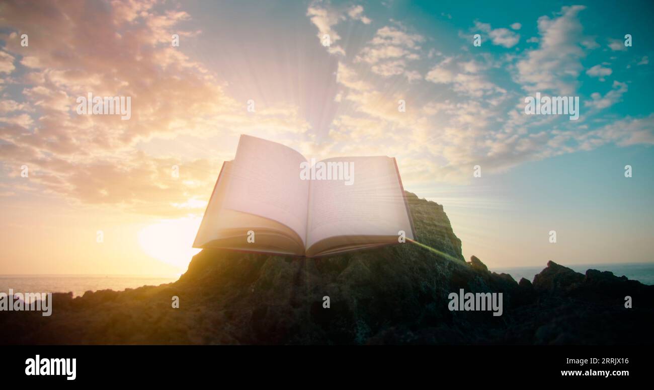 Die Heilige Bibel druckte ein offenes heiliges Buch vor natürlichem Hintergrund des Sonnenuntergangs. Felsiger Strand am Meer. Papierseiten leuchten. Beleuchteter Text in der antiken Schrift [M] Stockfoto