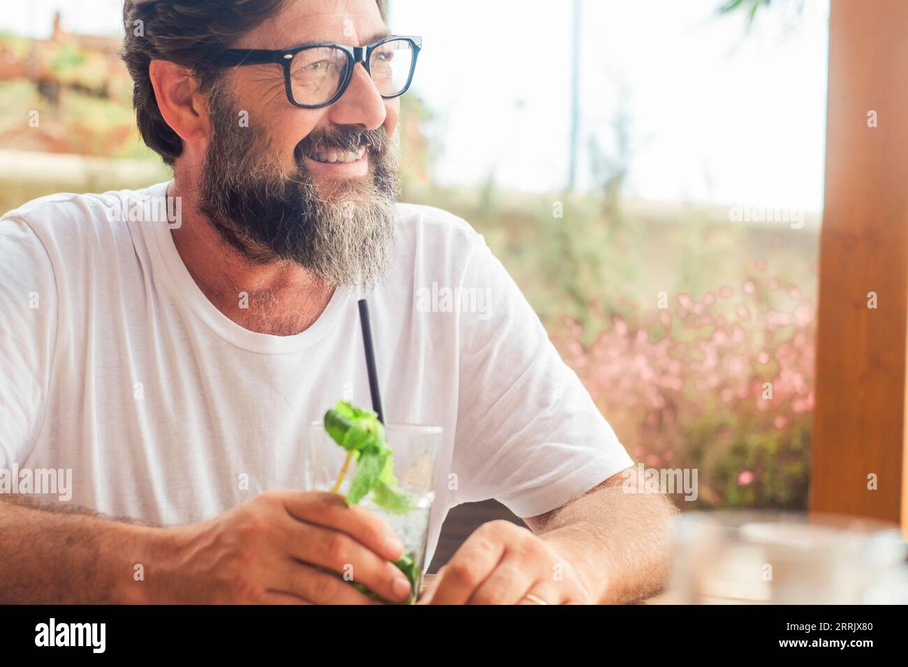 Porträt eines ruhigen glücklichen erwachsenen Mannes, der Mojito-Cocktail in der Café-Bar in den Sommerurlaubsferien im Freien trinkt. Touristen genießen Entspannung. Ein reifer Mann lächelt am Tisch Stockfoto
