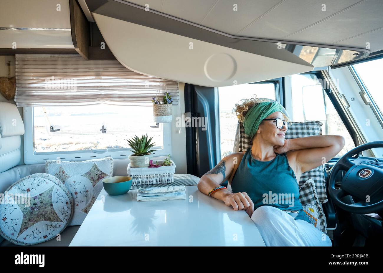 Eine junge Reisende Frau genießt die Zeit und entspannt sich im modernen Wohnmobil. Vanlifer Smile sitzt auf dem Fahrersitz und blickt auf das Ziel. Sommer Road Trip Urlaub Abenteuer weiblich - trendiges Leben Stockfoto