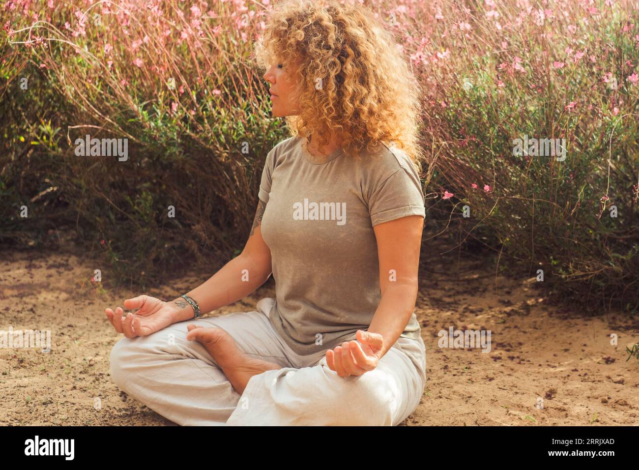 Outdoor-Meditationsübung für positiven Lebensstil und Wohlbefinden. Menschen genießen Yoga-Routine sitzend auf dem Boden in der Nähe von Blumen.nette gesunde Frau in Lotus-Position und geschlossene Augen. Zenlike Leben Stockfoto