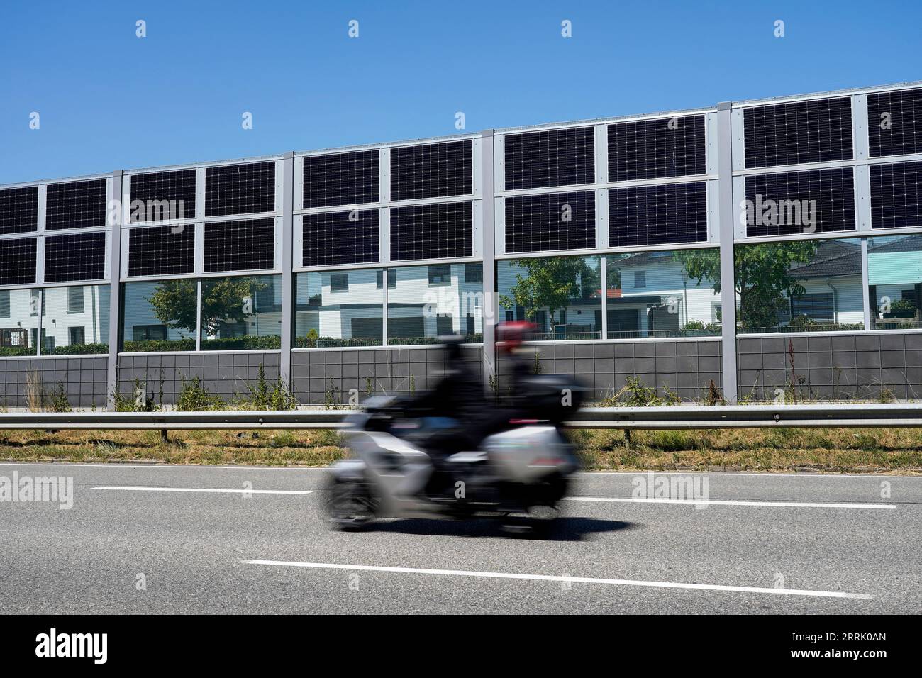 Deutschland, Bayern, Oberbayern, Neuötting, Wohnsiedlung, davor Schallmauer mit Photovoltaik, Straße, vorbeifahrendes Motorrad Stockfoto