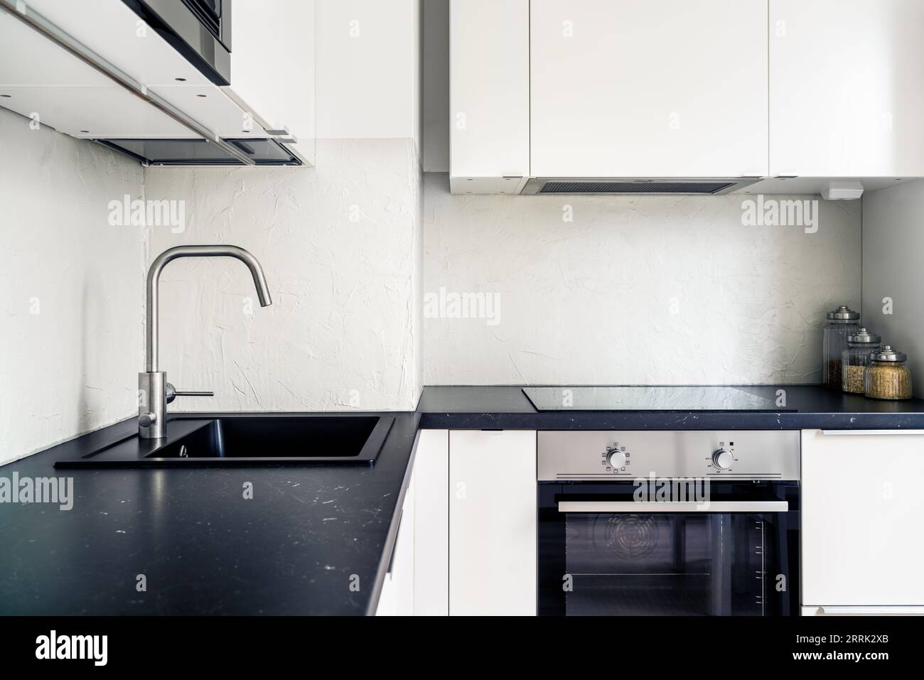 Kücheneinrichtung. Modernes Design in weiß und Schwarz. Skandinavischer minimalistischer Lebensstil. Induktionskocher und Herd, Elektroofen in neuer Wohnung. Stockfoto