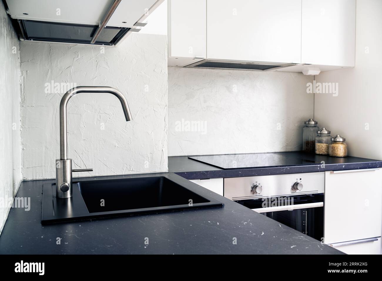 Küchenarbeitsplatte, Wasserhahn, Wasserhahn und Waschbecken. Weiß und schwarz skandinavisches Innendesign in modernen Apartments und Wohnungen. Induktionskochfeld. Stockfoto