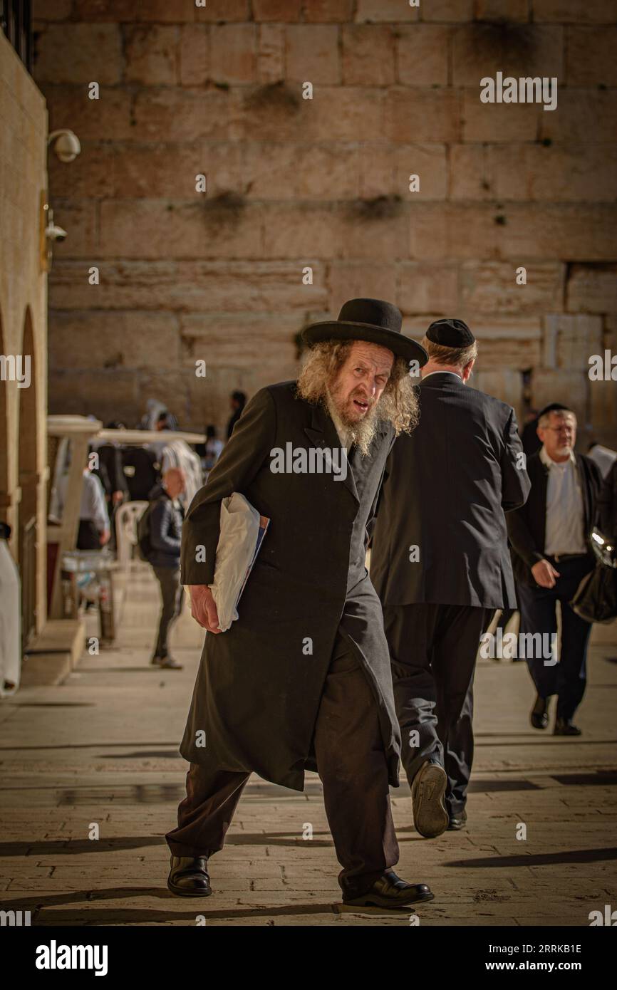 Ein elegant aussehender Gentleman mit einem stylischen langen Hut läuft tagsüber eine belebte Straße entlang Stockfoto