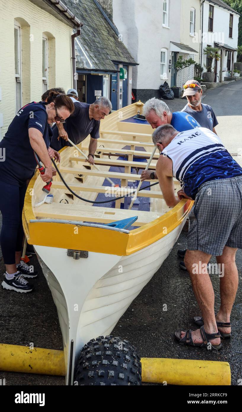 Mitglieder des Rame Gig Club gehen an einem heißen Septembertag in den Schatten, um das Maker Wave Boot am Cawsand Square zu warten Stockfoto