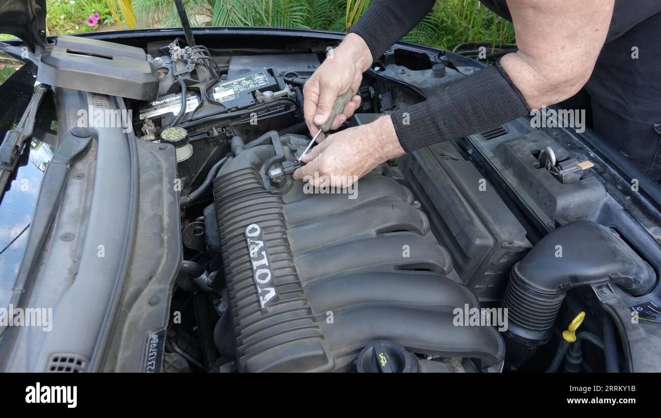 Vista, CA USA - 3. September 2023: Nahaufnahme der Hände eines alten Mannes, als er den Ansaugkrümmer eines Volvo S40 aus dem Jahr 2007 entfernt, um zu den Zündkerzen zu gelangen Stockfoto