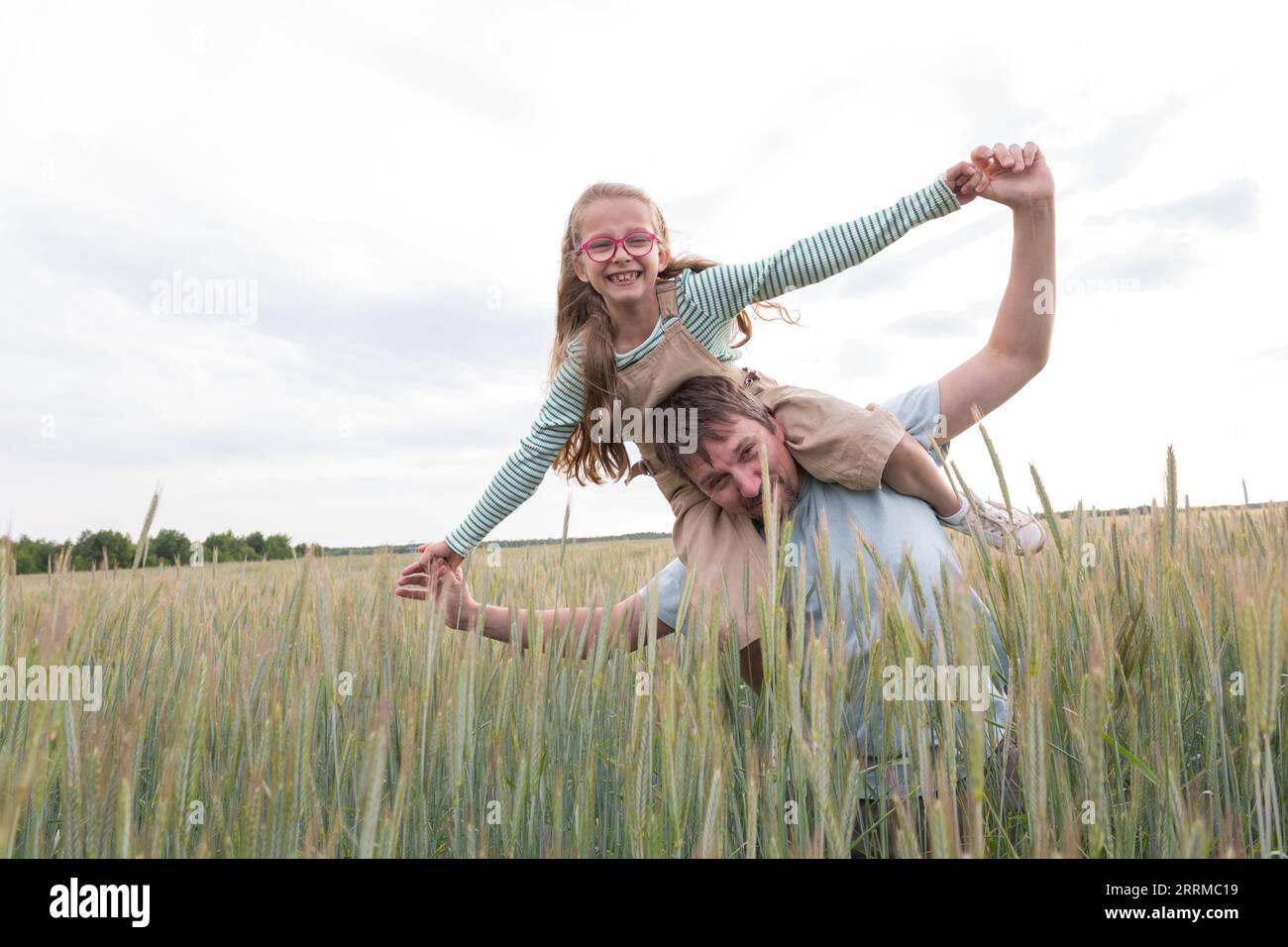 Ein Mädchen und ihr Vater sind glücklich und spielen vor dem Hintergrund eines landwirtschaftlichen Feldes. Stockfoto