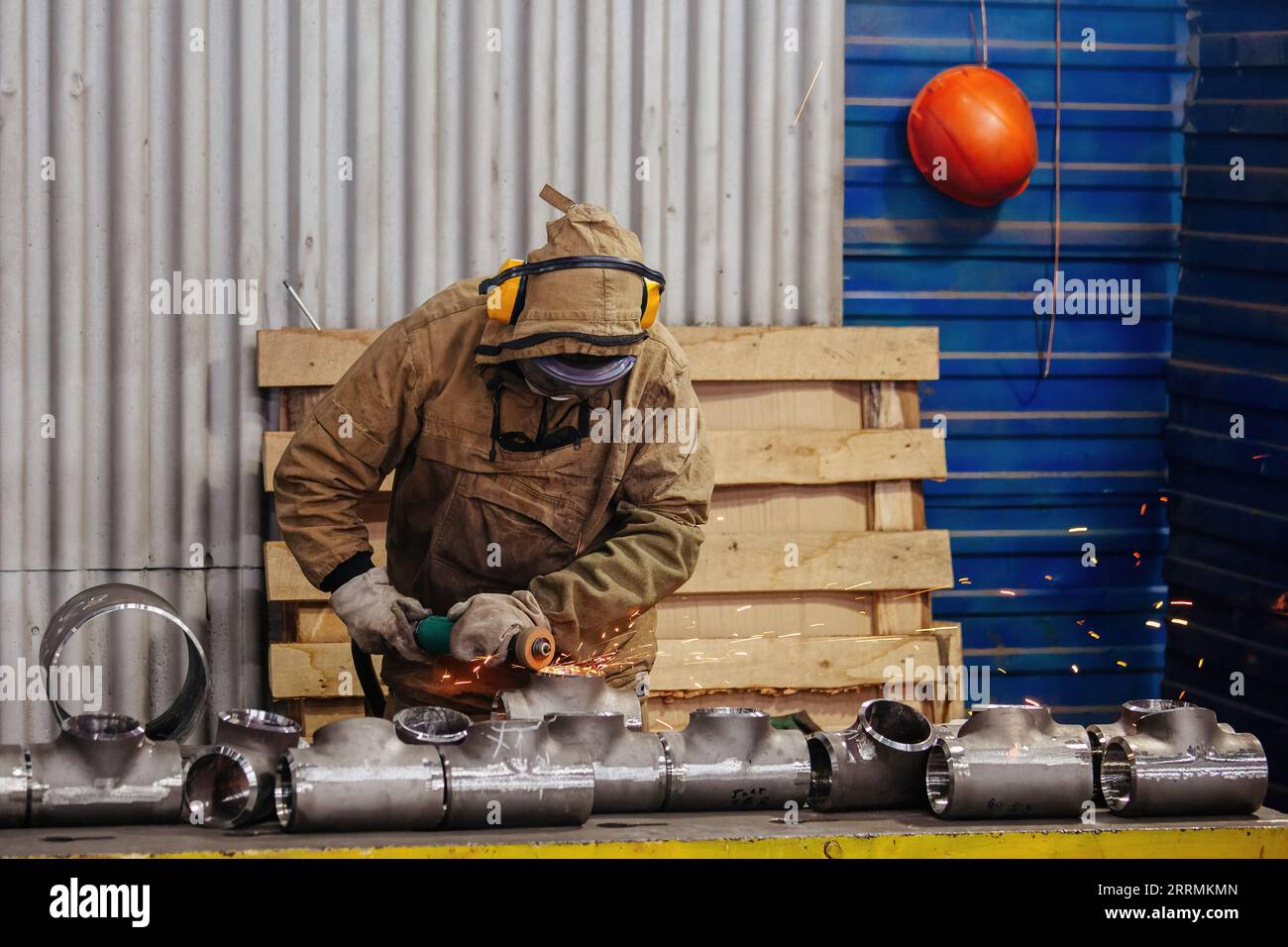 Männlicher Arbeiter, der T-förmige Rohrteile im Werk schleift. Stockfoto
