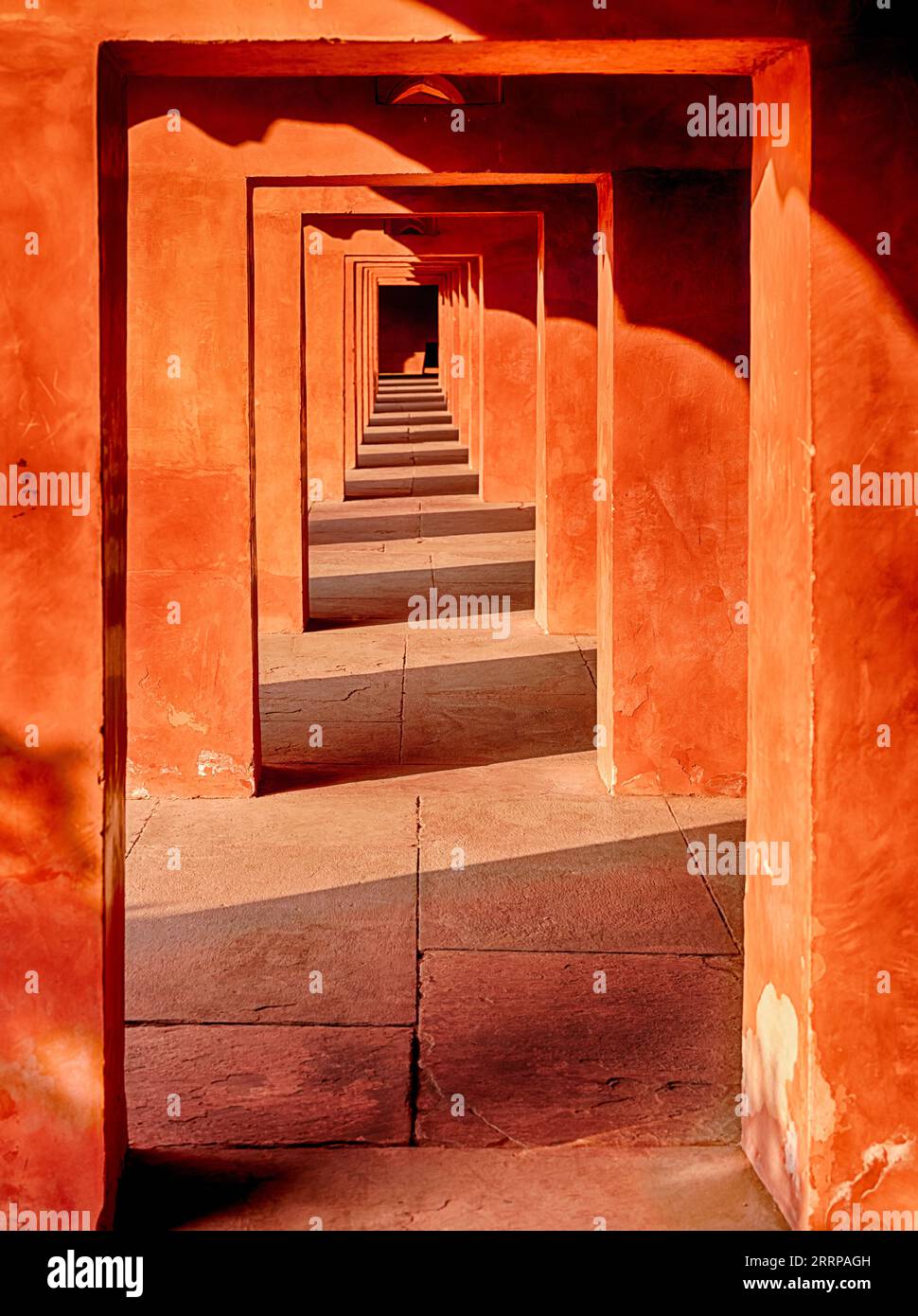 Ein Korridor aus rotem Sandstein im Nachmittagslicht hebt wechselnde Licht- und Schattenbänder im Taj Mahal-Komplex in Agra, Indien, hervor. Stockfoto