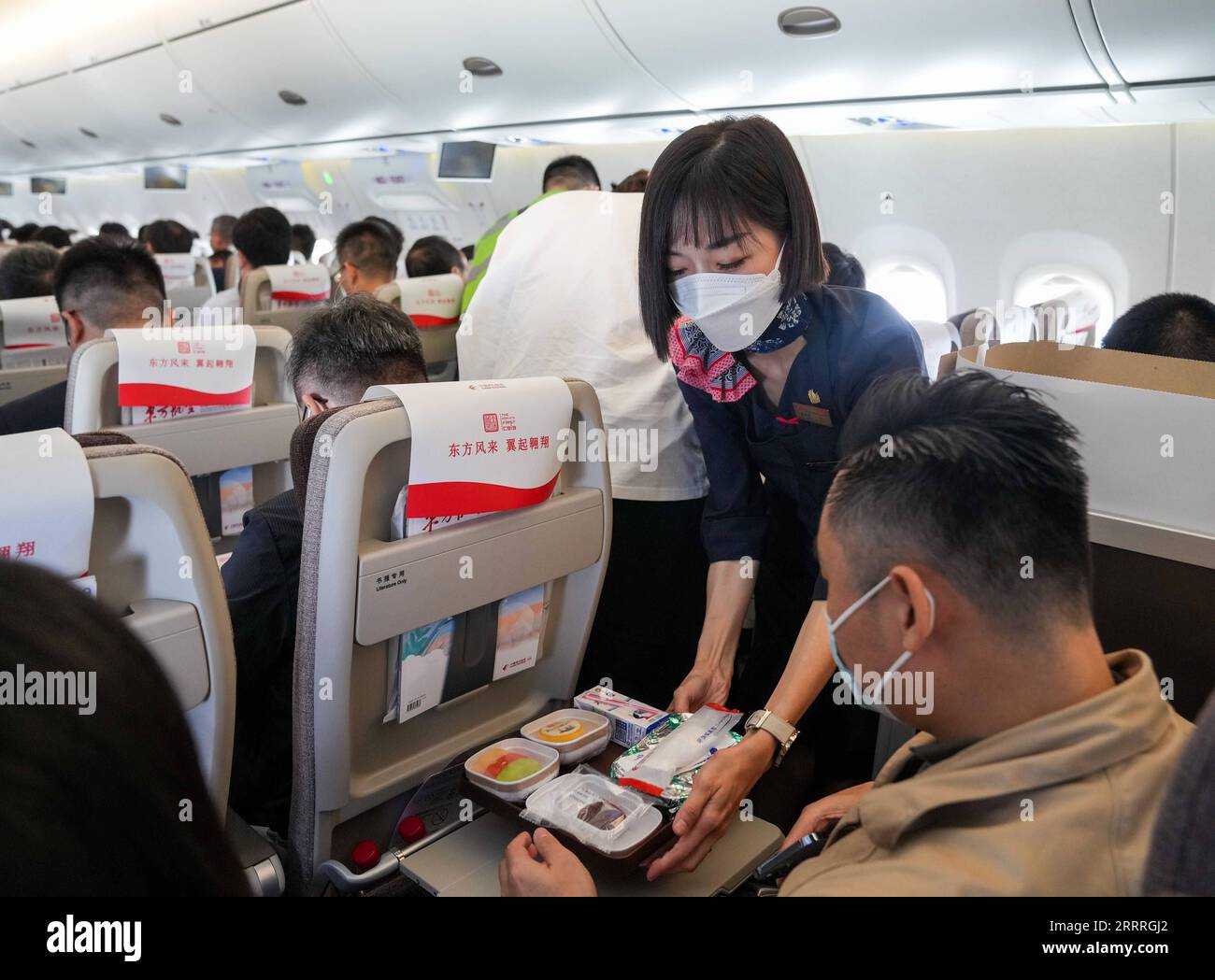 China, neues Passagierflugzeug C919 in Peking 230528 -- SHANGHAI, 28. Mai 2023 -- Ein Flugbegleiter serviert einem Passagier an Bord eines großen Passagierflugzeugs C919, Chinas erster selbst entwickelter Kofferraumjet, am 28. Mai 2023 von Shanghai nach Peking eine Mahlzeit. Die C919, Chinas selbstentwickeltes großes Passagierflugzeug, absolvierte am Sonntag ihren ersten kommerziellen Flug von Shanghai nach Peking und feierte damit ihren offiziellen Eintritt in den zivilen Luftverkehr. EyesonSciCHINA-PASSENGER AIRCRAFT-C919-ERSTER KOMMERZIELLER FLUG CN DingxTing PUBLICATIONxNOTxINxCHN Stockfoto