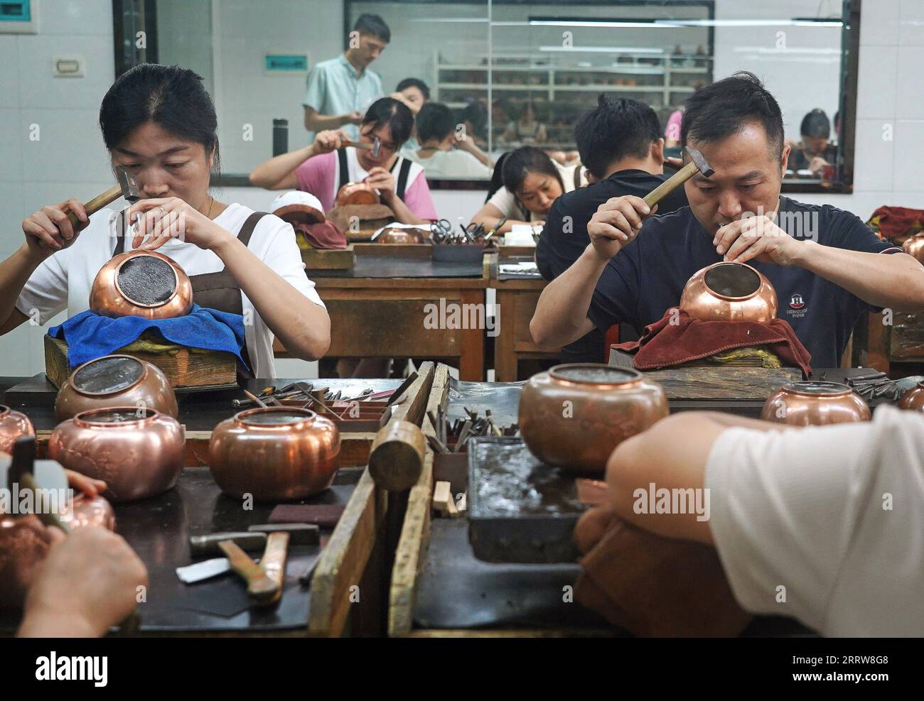 230815 -- NANCHANG, 15. August 2023 -- Handwerker fertigen Teekannen mit Kupferstich in Huang Junjuns Unternehmen in Guixi, ostchinesische Provinz Jiangxi, 13. Juli 2023. Kupferstich oder Kupferschnitzerei, ein Handwerk der Verwendung von Messern zum Schnitzen von Mustern auf Kupferwaren, hat eine Geschichte von etwa 1.000 Jahren. Im Jahr 2021 wurde der Kupferstich Guixi als eines der immateriellen Kulturgüter auf nationaler Ebene aufgeführt. Das Handwerk benötigt über 150 verschiedene Arten von Messern und ein Dutzend Schnitzkunst, um ein komplettes Kunstwerk zu erstellen, und die Kupferwaren müssen mehr als 100.000 Mal hämmern, bevor sie gedreht werden Stockfoto