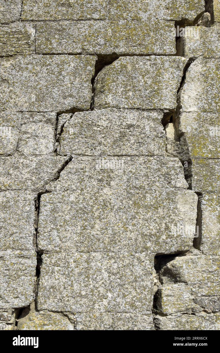 Eine alte, mit Moos bedeckte Steinmauer mit tiefen Rissen und eingestürzten Steinen. Große diagonale Risse an der alten Wand. Leerzeichen kopieren. Selektiver Fokus. Stockfoto Eine alte, mit Moos bedeckte Steinmauer mit tiefen Rissen und eingestürzten Steinen. Große diagonale Risse an der alten Wand. Leerzeichen kopieren. Selektiver Fokus. Stockfoto