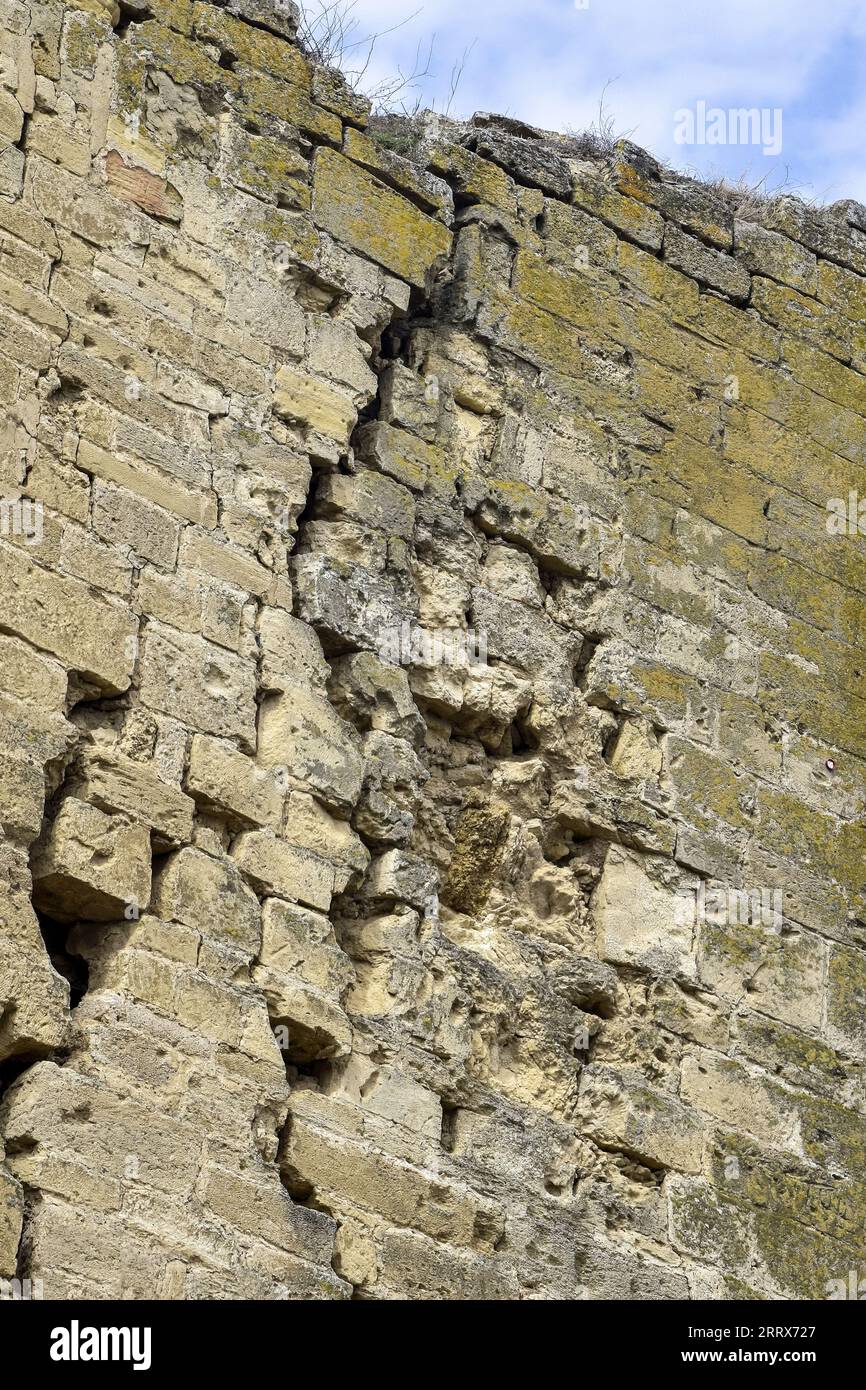 Eine alte, mit Moos bedeckte Steinmauer mit tiefen Rissen und eingestürzten Steinen. Große diagonale Risse an der alten Wand. Leerzeichen kopieren. Selektiver Fokus. Stockfoto Eine alte, mit Moos bedeckte Steinmauer mit tiefen Rissen und eingestürzten Steinen. Große diagonale Risse an der alten Wand. Leerzeichen kopieren. Selektiver Fokus. Stockfoto