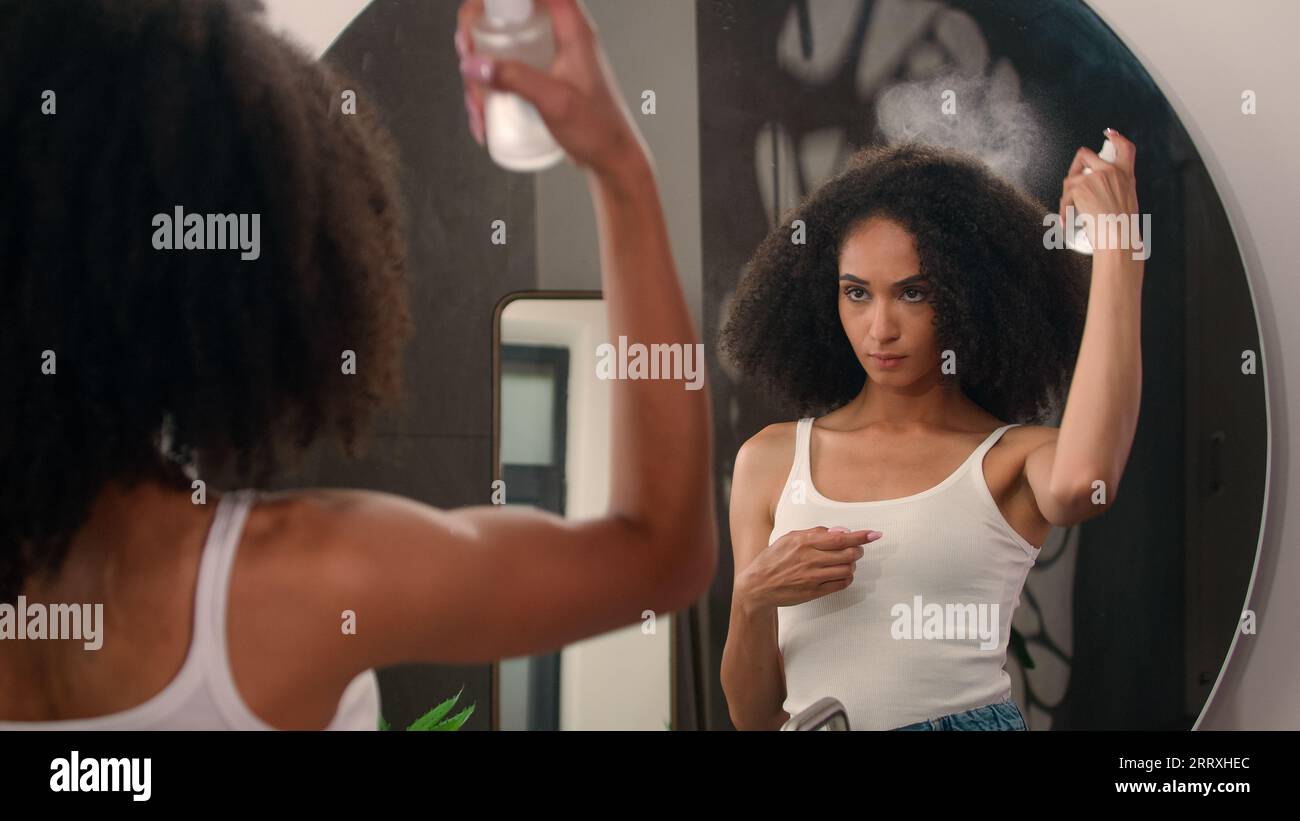 Spiegelreflexion im Badezimmer afroamerikanische Frau schönes Mädchen mit wunderschönen lockigen Haarlocken, die Thermalwasser auf die Haarkosmetik sprühen Stockfoto