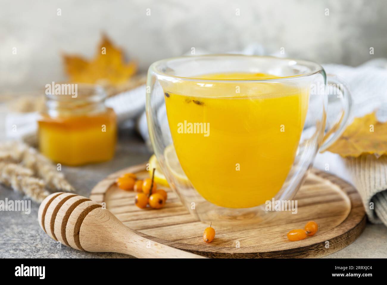 Entspannung und Kräutermedizin. Heißer Kräuter-Vitamin-Sanddorn-Tee in einer Glasschale mit frischen Sanddornbeeren, Honig und Zitrone auf einem Steintisch Stockfoto