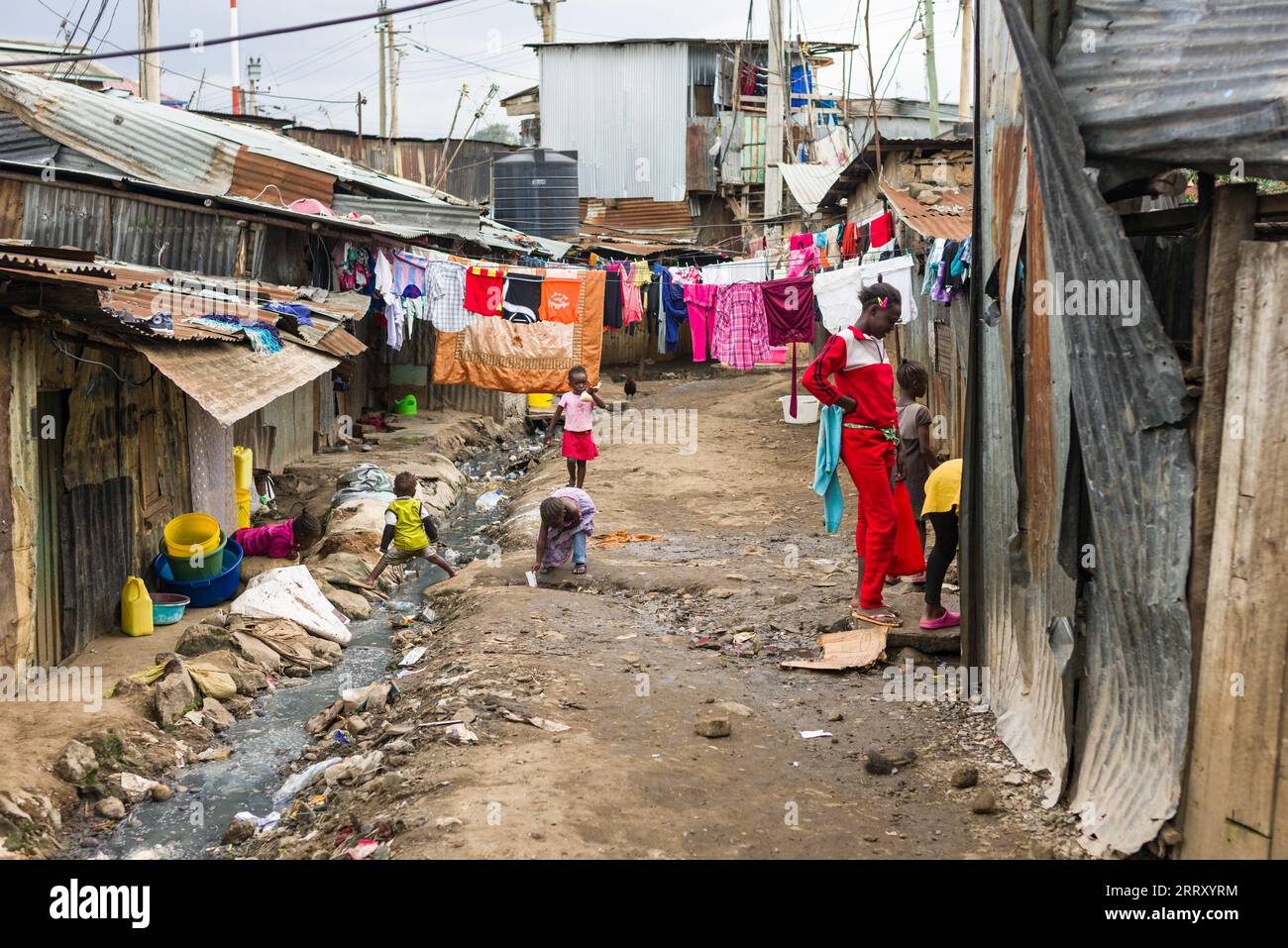 Blick auf einen Seitenweg mit gewellten Metallhütten, mit Kindern, die neben der offenen Kanalisation spielen, Mathare Slum, Kenia Stockfoto