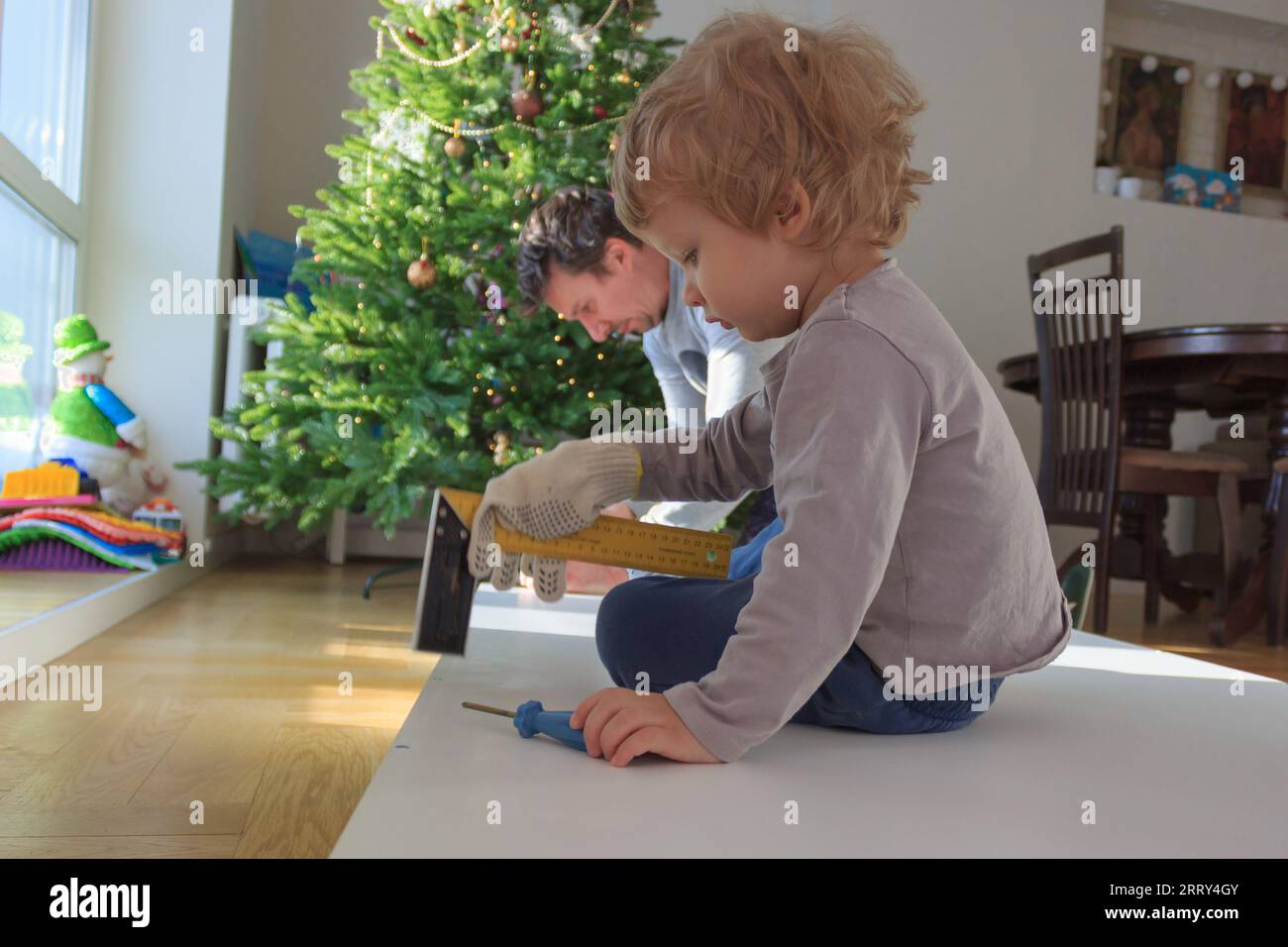 Hausrenovierung zum Selbermachen: Vater und Kind reparieren gemeinsam Möbel am Weihnachtsbaum. Stockfoto