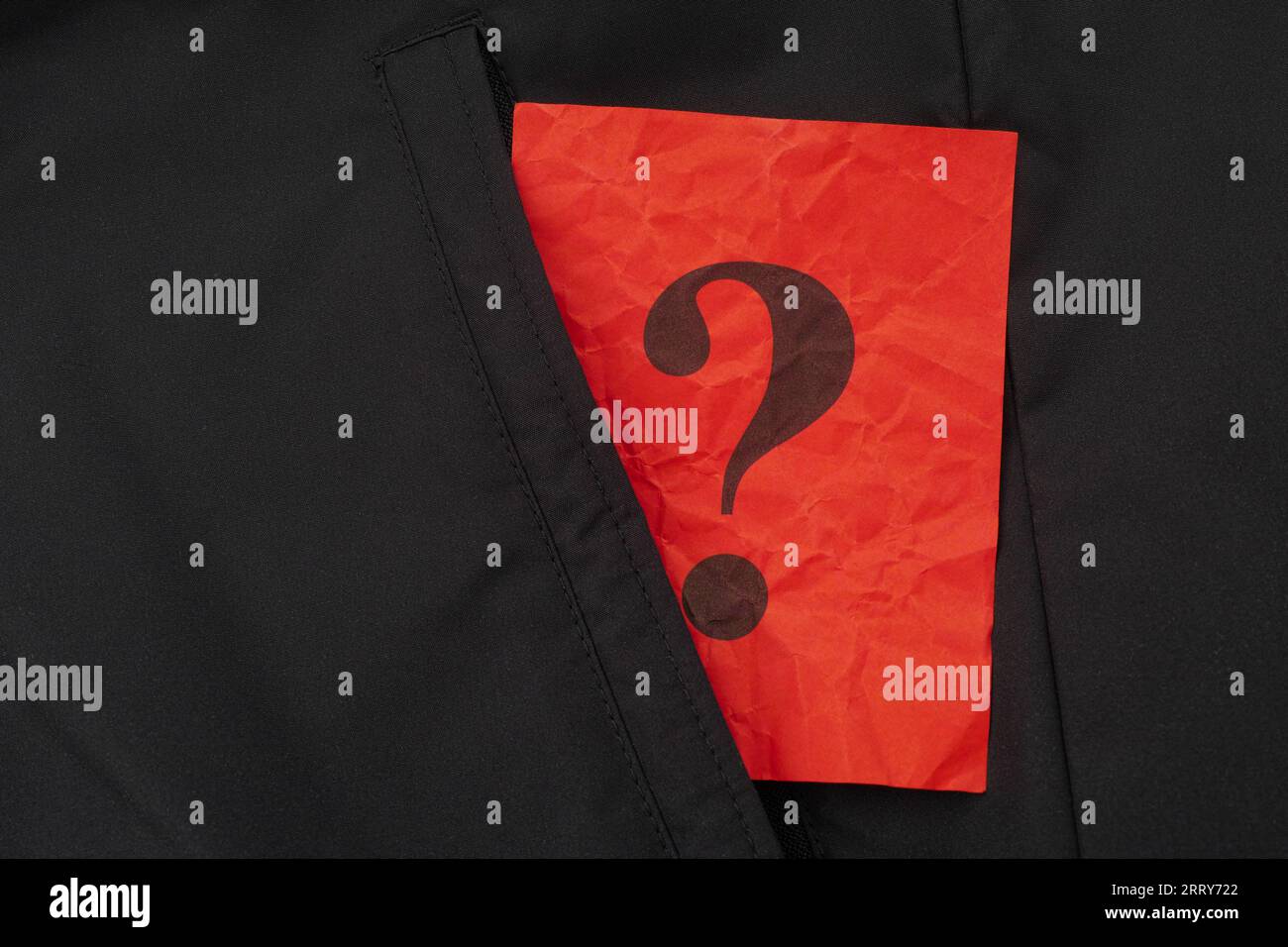 Ein zerknittertes rotes Stück Papier mit einem Fragezeichen, das aus der Tasche einer schwarzen Jacke ragt. Nahaufnahme. Stockfoto