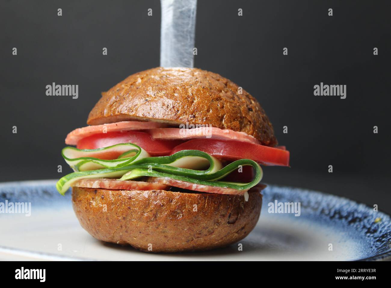 Ein Buchweizen-Brot-Sandwich-Burger aus Schinkenwurst und Gurke und Tomatengemüse auf einem Teller auf einem ernomphone mit einem Platz für den Text. Schnell hausgemacht Stockfoto