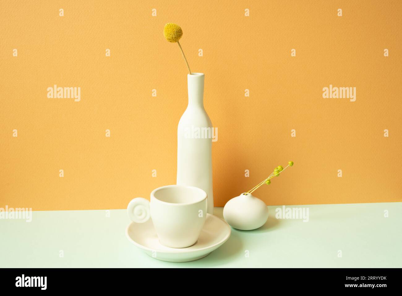 Minimalistisch weiße Kaffeetasse aus Keramik und Blumenvase auf minzgrünem Tisch. Orangefarbener Hintergrund Stockfoto