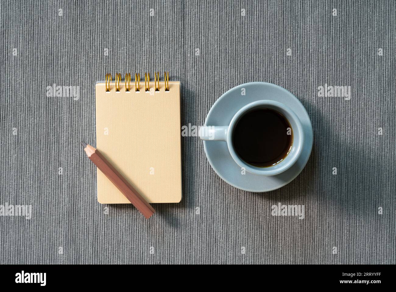 Brauner Notizblock, farbiger Bleistift, Tasse Kaffee auf grauem Stoffhintergrund. Draufsicht, Kopierbereich. Arbeitsbereich Stockfoto