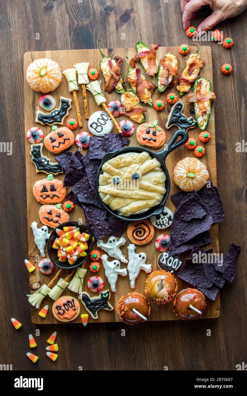 Eine Hand, die ein Charcuterie-Board mit Halloween-Themen mit gruseligen Leckereien verziert. Stockfoto