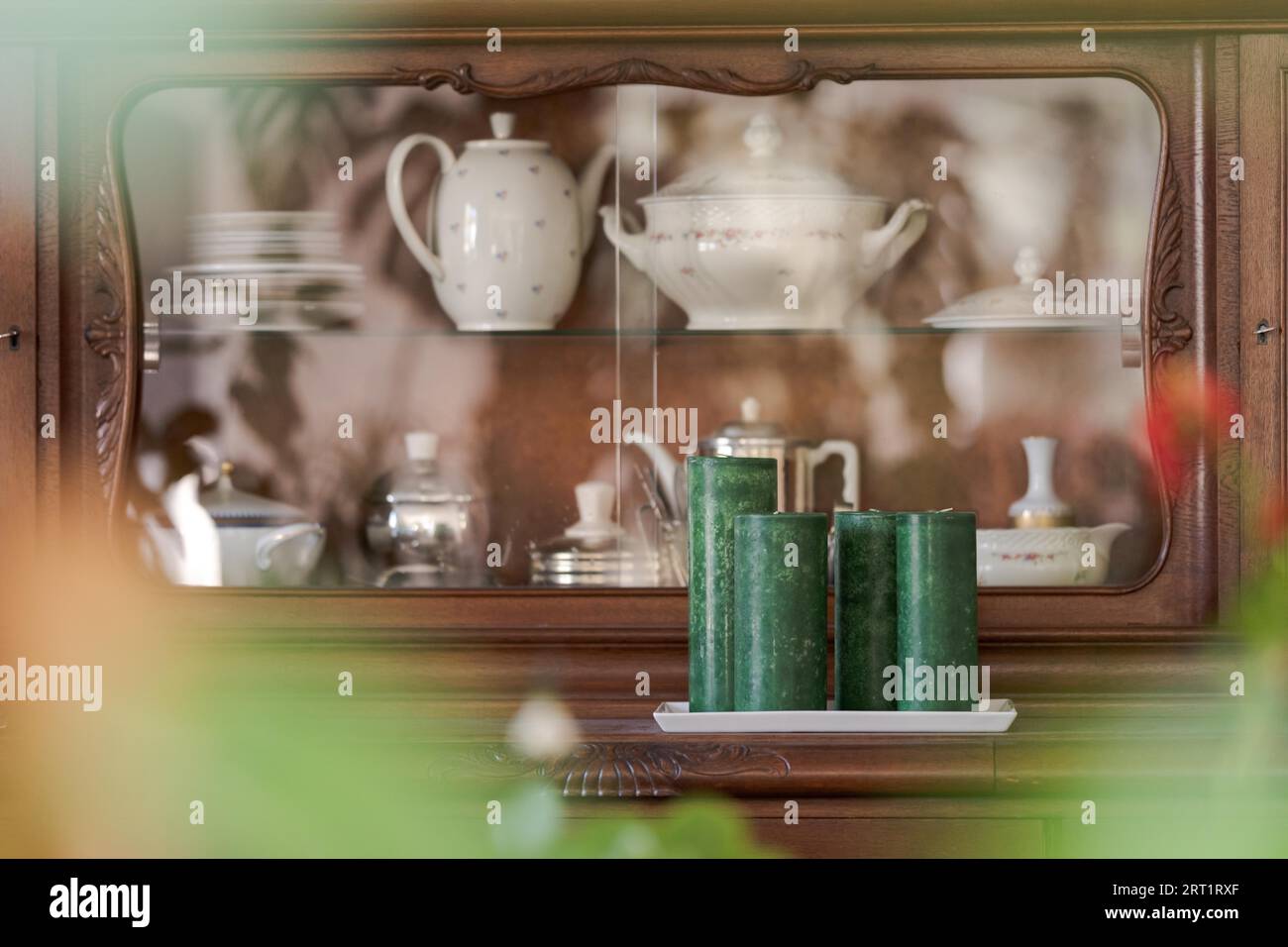 Vor dem alten Sideboard aus Holz, gefüllt mit grandmotherÂ Teekannen und Tellern, durch den verschwommenen Vorder von Zimmerpflanzen gesehen Stockfoto