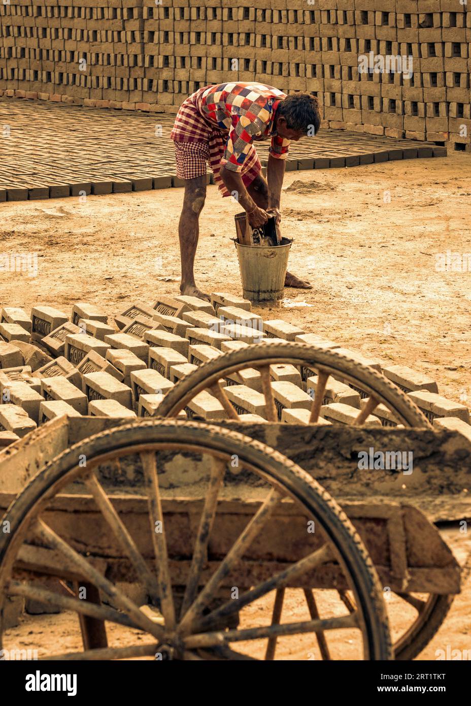 In West-Bengalen, Indien, reinigt ein ermüdeter Arbeiter sorgfältig Ziegelformen und schließt einen mühsamen Tag in einer traditionellen Ziegelsteinfabrik ab. Stockfoto