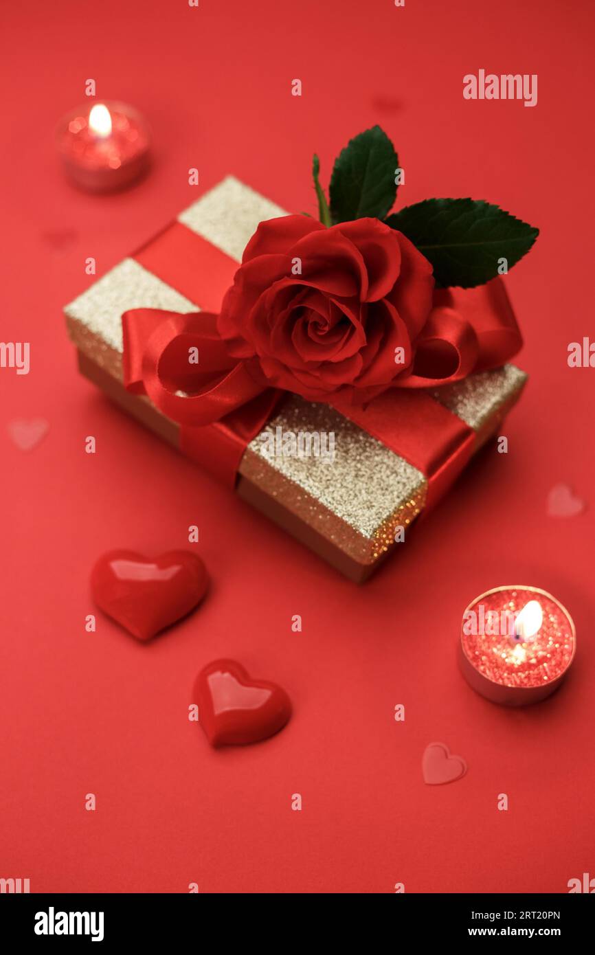 Goldene Geschenkbox mit Band und der Rose auf rotem Hintergrund, Valentinskarte oder Muttertagskarte Kopierraum flach liegend, vertikal Stockfoto