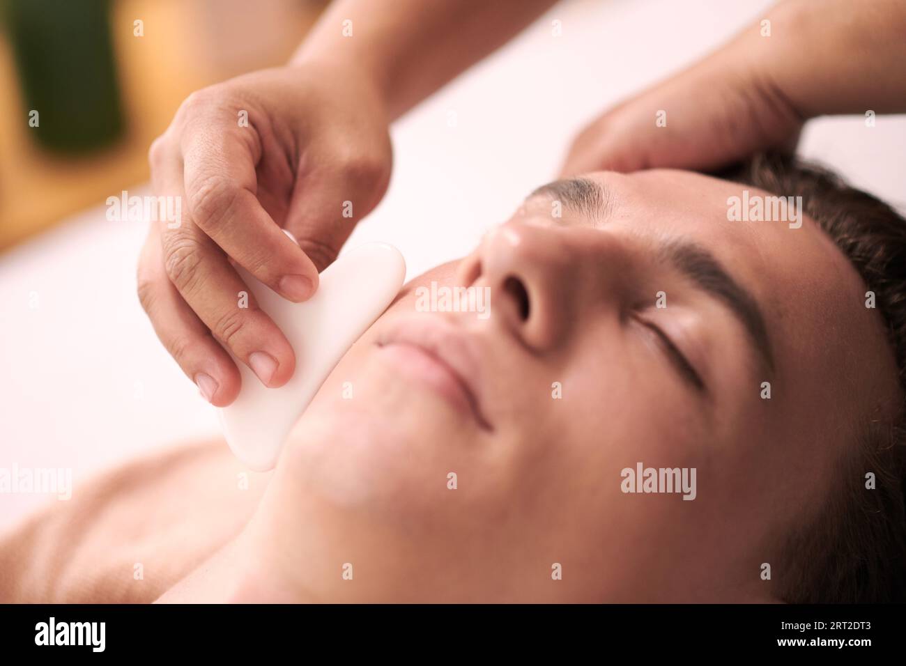 Cosmetologe mit Gua SHA bei der Gesichtsmassage des Menschen Stockfoto