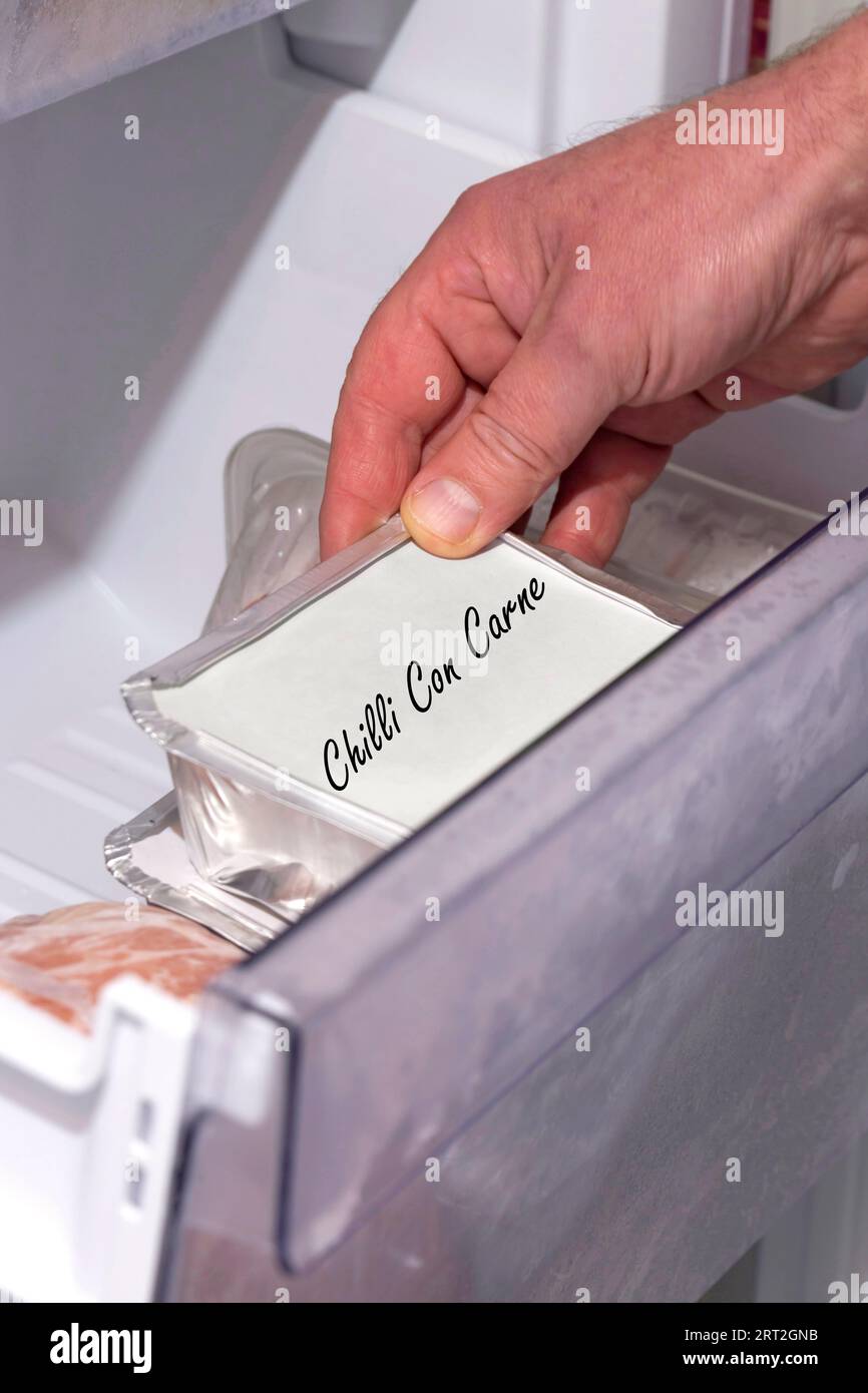 Mann, der hausgemachte gekochte Chili con Carne in einem Behälter mit Folienschale aus einer Tiefkühlschublade nimmt. Konzept zur Einsparung von Lebensmittelkosten Stockfoto