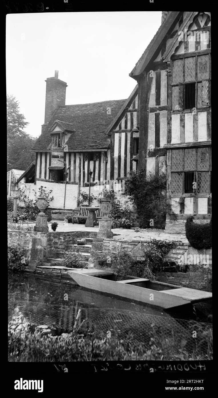 Huddington Court, Huddington, Wychavon, Worcestershire, 1940-1948. Ein Außenblick auf Huddington Court, mit einem Wasserkörper und einem gepflasterten Garten im Vordergrund. Auf dem Wasser liegt ein kleines Holzboot neben einer Treppe, die zum gepflasterten Garten und zum Haus führt. Das Bild zeigt möglicherweise die Ostseite des Hauses, wobei der Wasserkörper Teil des Grabens ist, der das Anwesen umgibt. Huddington Court ist ein Haus aus dem 16. Jahrhundert, das einst der Familie Wintour gehörte, die am Gunpowder Plot beteiligt war. Wintour wird auch Wyntour geschrieben. Stockfoto