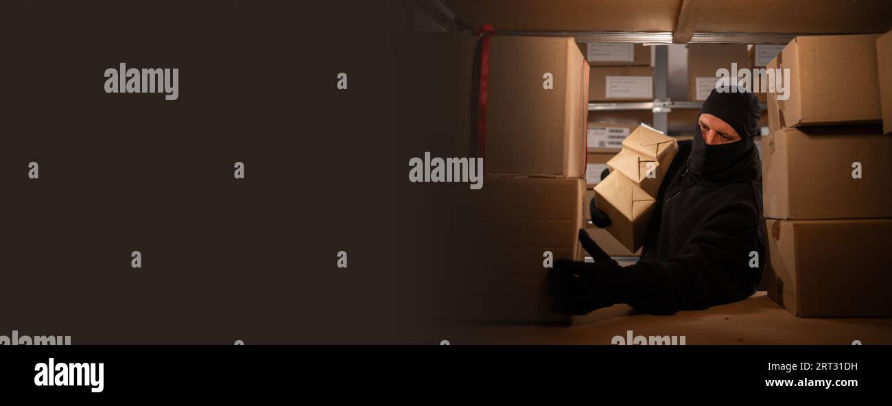 Dieb trägt Handschuhe und stiehlt in einem Lager im Dunkeln Warenschachteln. Zur Problematik des Diebstahls von Postpaketen. Stockfoto