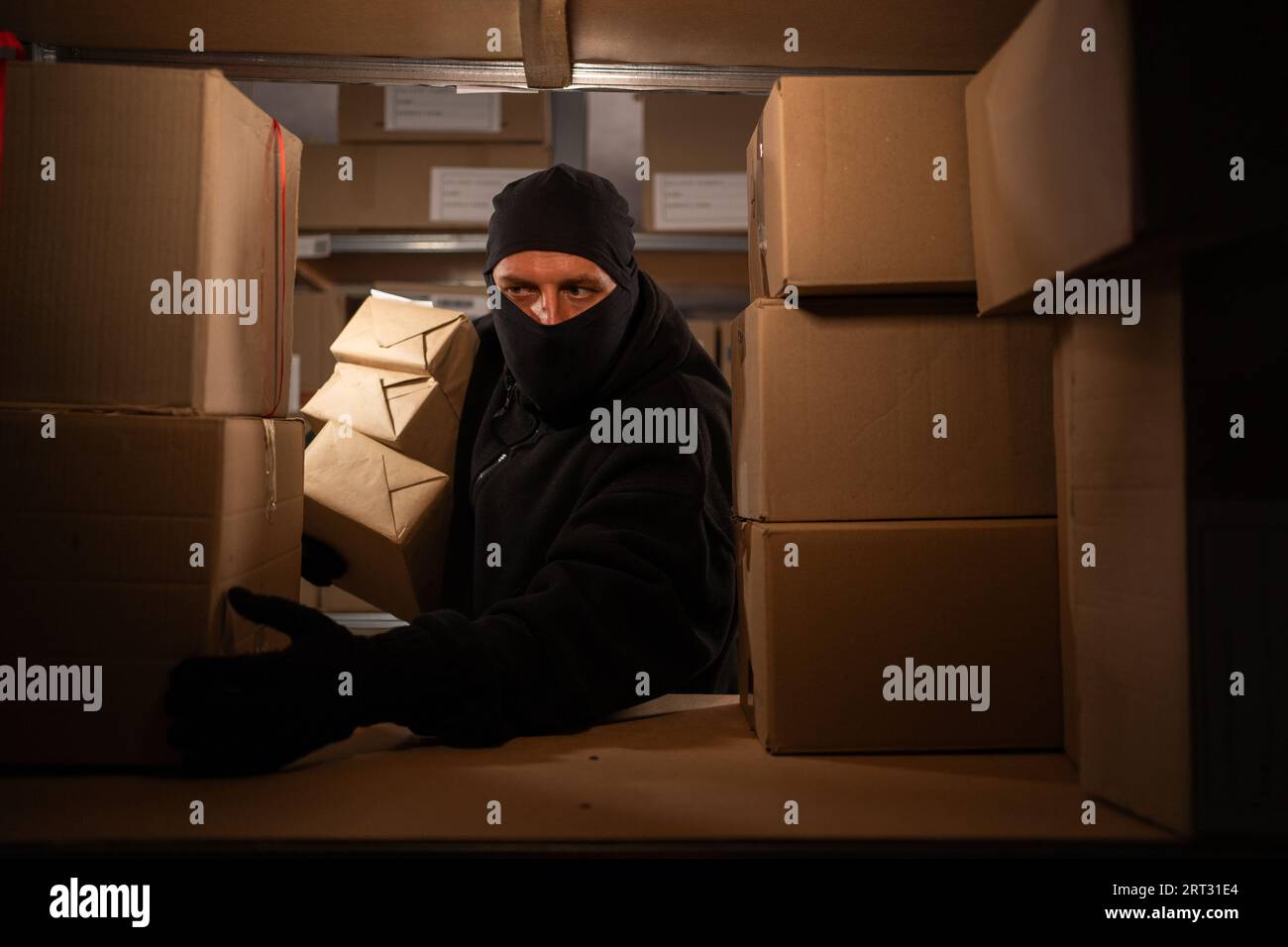 Dieb trägt Handschuhe und stiehlt in einem Lager im Dunkeln Warenschachteln. Zur Problematik des Diebstahls von Postpaketen Stockfoto
